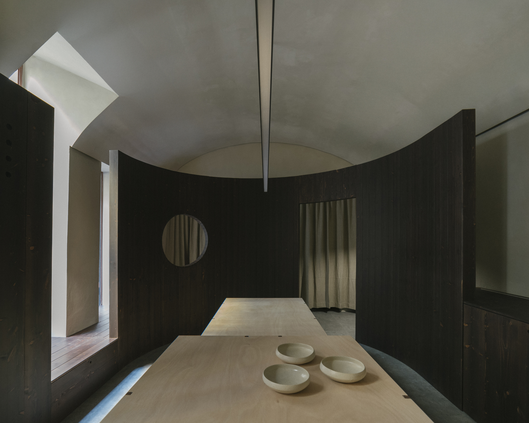 Interior room with dark timber partition, circular opening, and plywood table holding three ceramic bowls