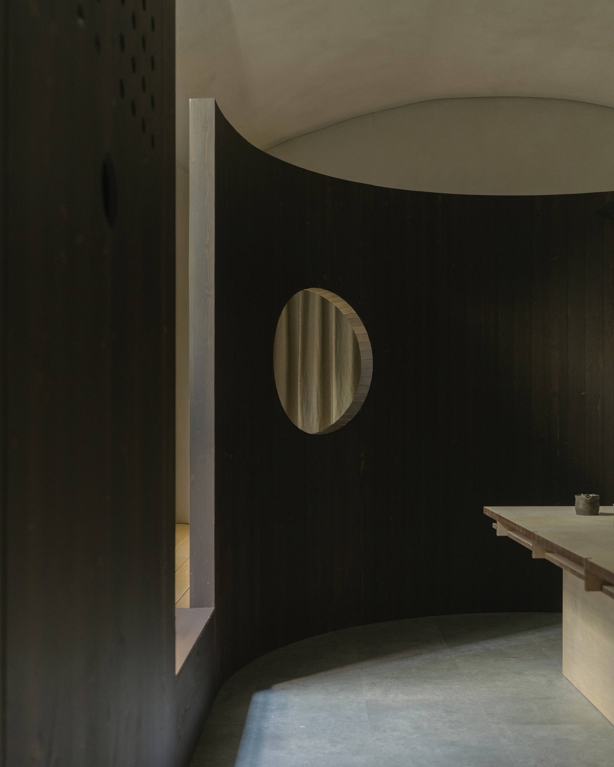Curved partition wall with circular window reflecting curtains, meeting white plastered wall at corner in shadow