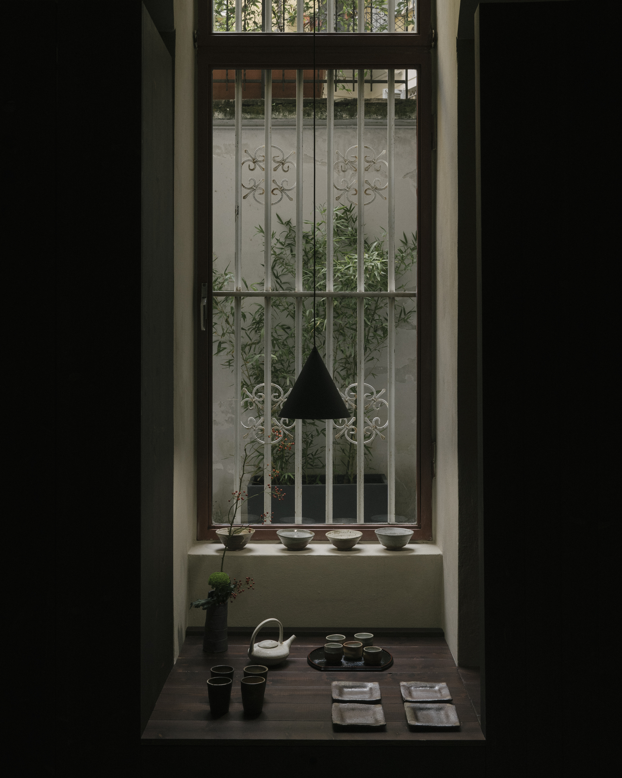 Low table set for tea in front of window with decorative metal grille and planted courtyard beyond