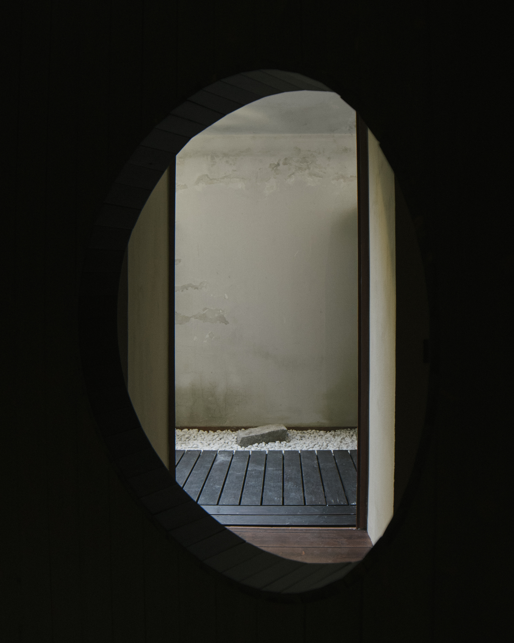 View through oval portal showing timber decking, white gravel bed, and rendered wall in daylight