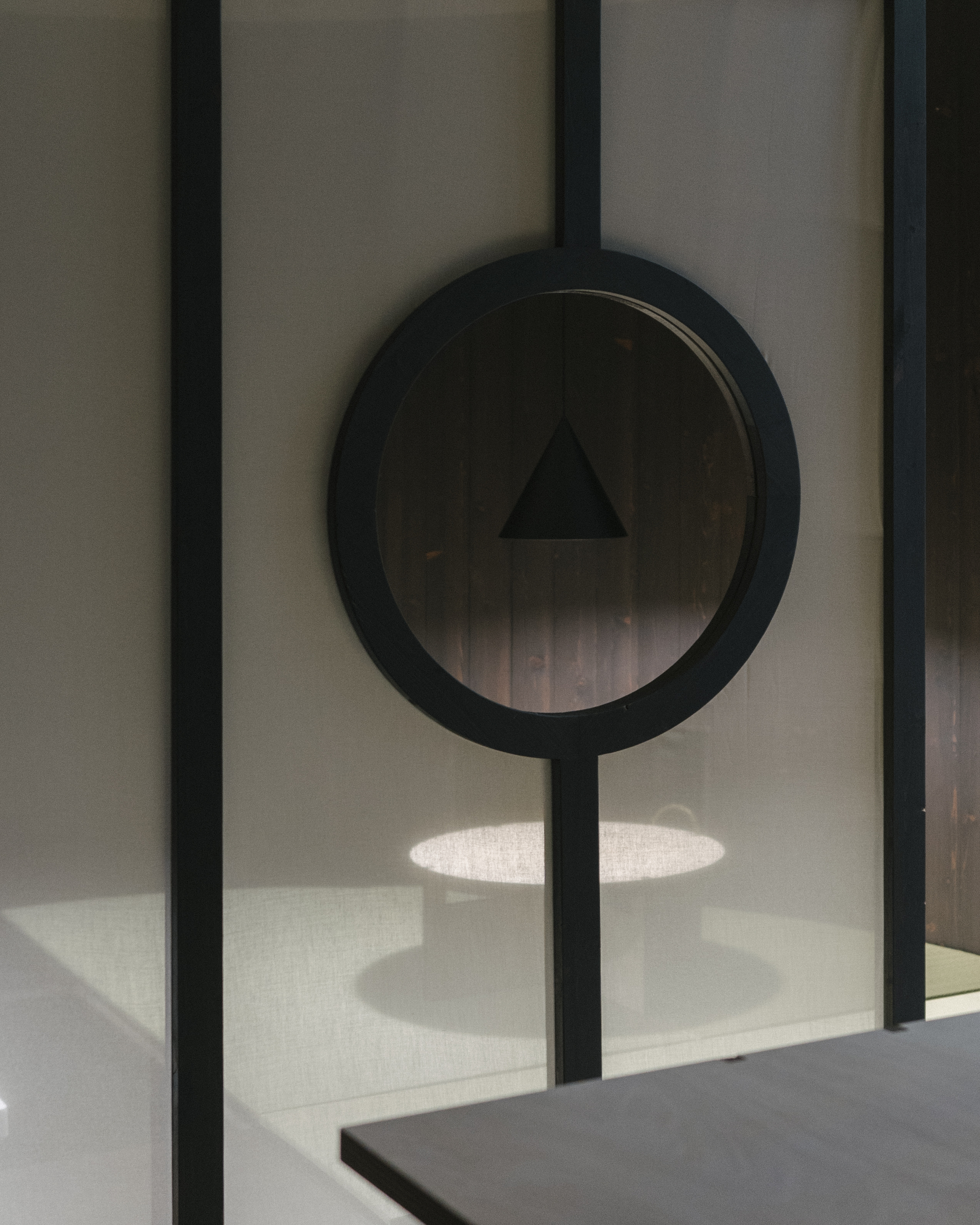 Circular mirror mounted on vertical steel bar casting shadow over concrete counter below