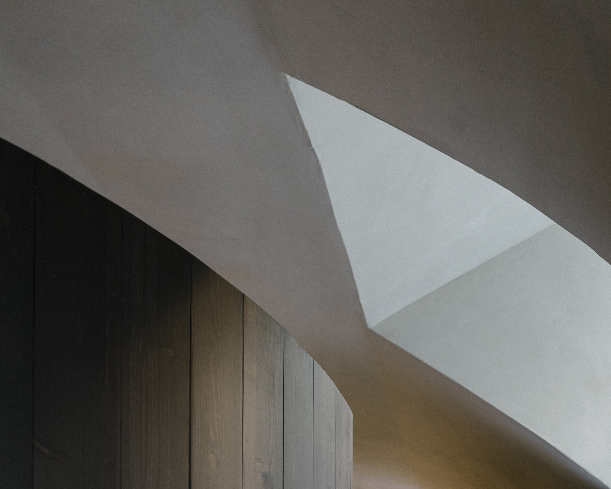 Triangular skylight piercing white plaster ceiling above dark timber wall paneling