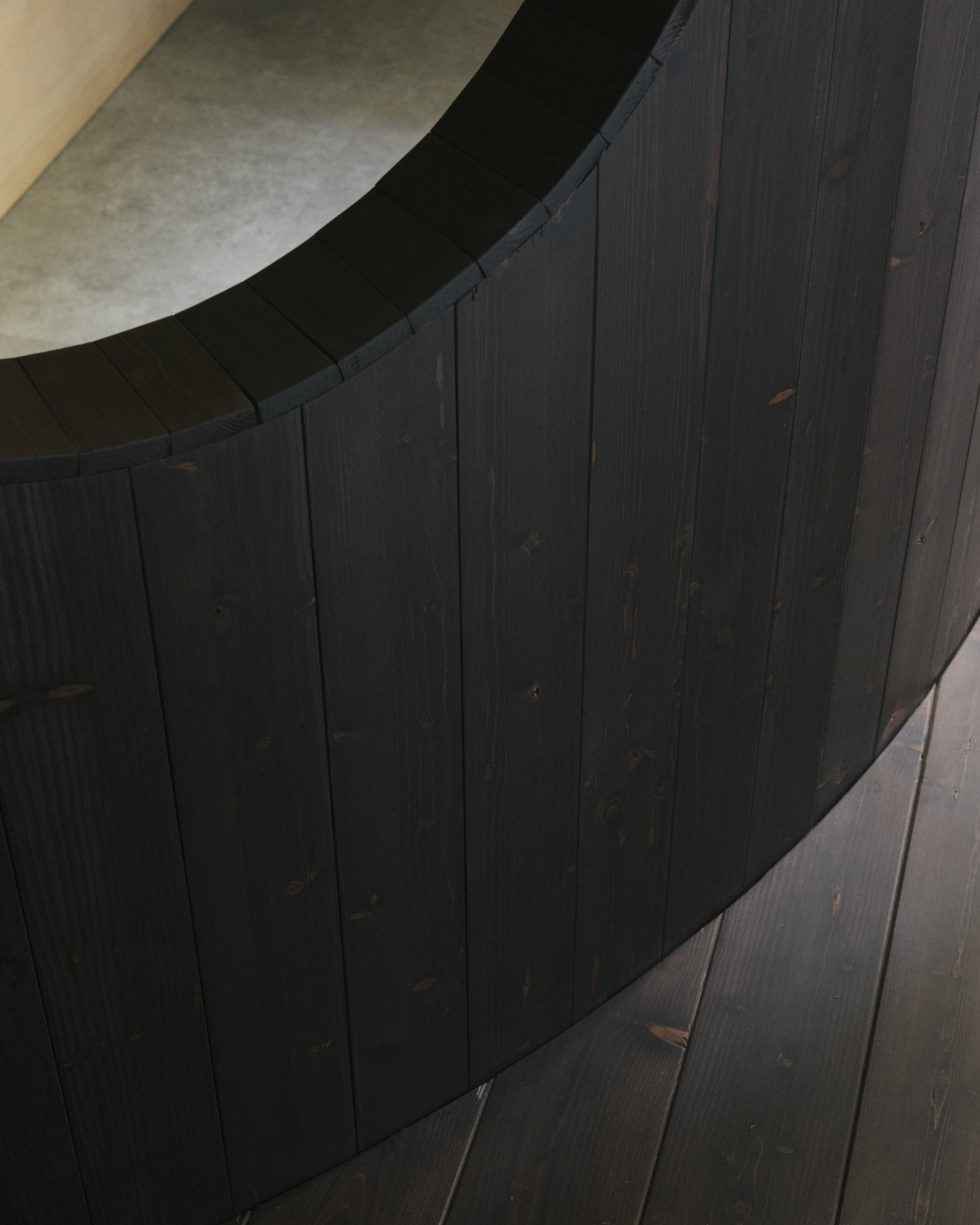 Close-up of curved charred timber wall with vertical planks meeting arched plaster ceiling