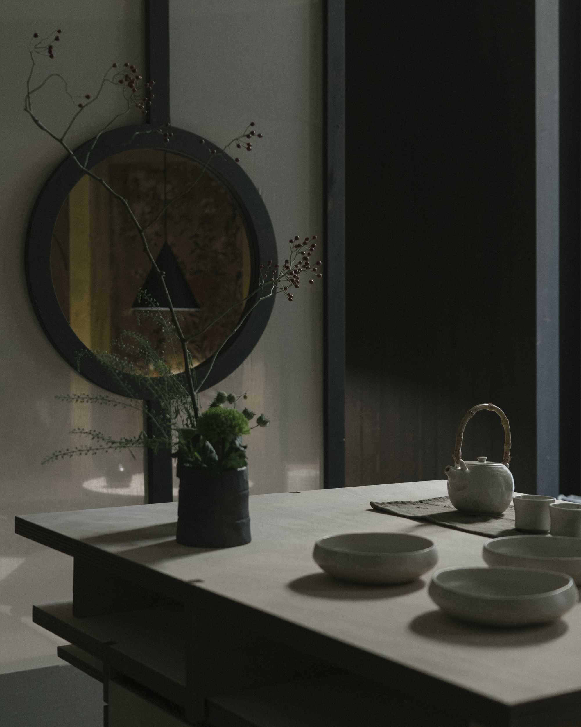 White countertop with ceramic tea set and dried branches reflected in a round mirror