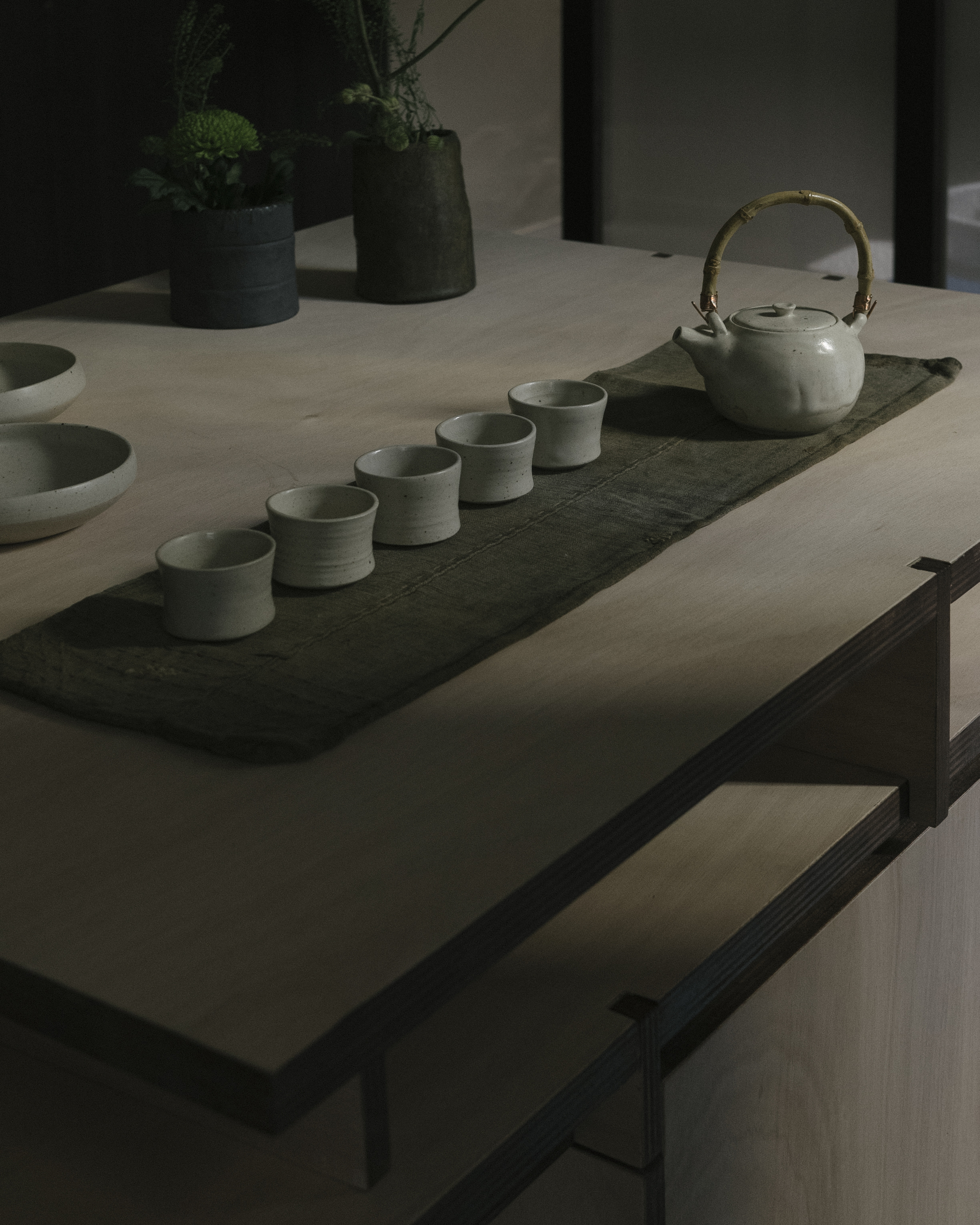 Tea ceremony arrangement with ceramic cups and teapot on a dark stone runner