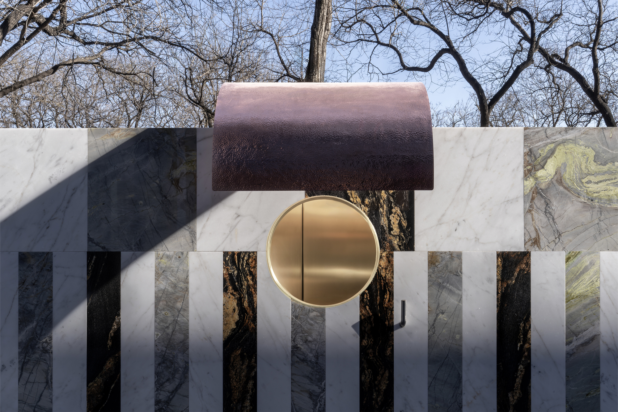 Close-up of the circular brass disc set within white marble panels beneath the copper overhang canopy