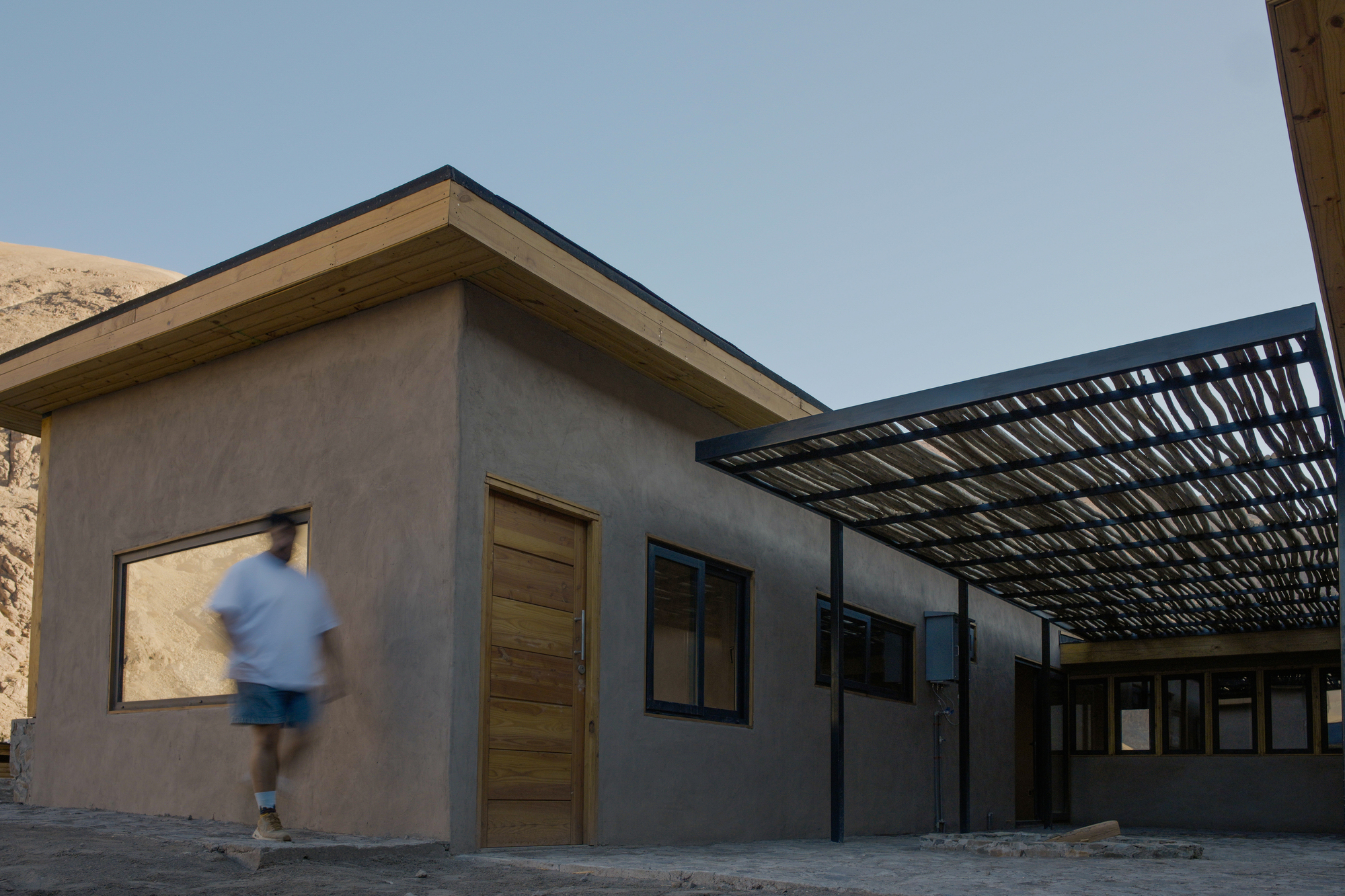 Exterior wall with timber door and metal lattice pergola as a person walks past
