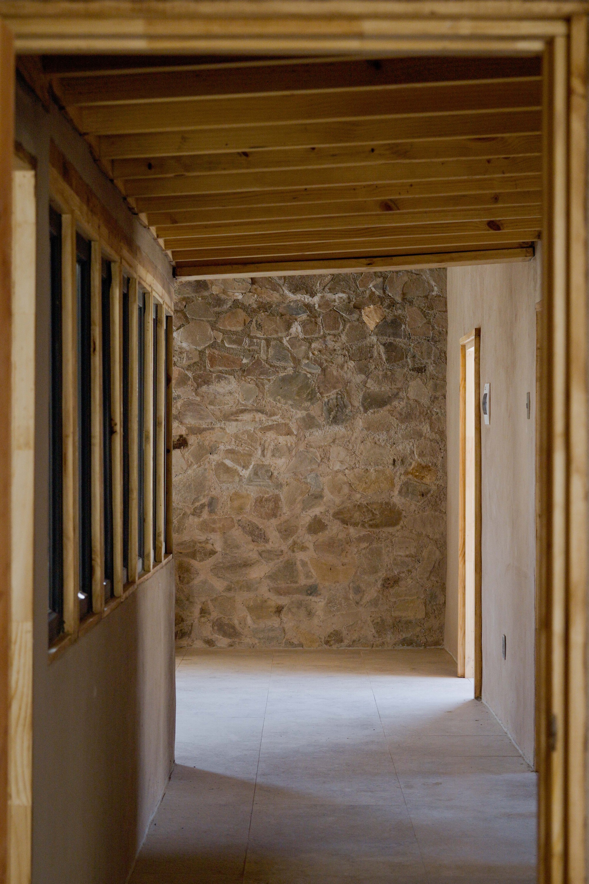 Interior corridor with exposed timber ceiling beams, stone wall, and timber slat partition wall