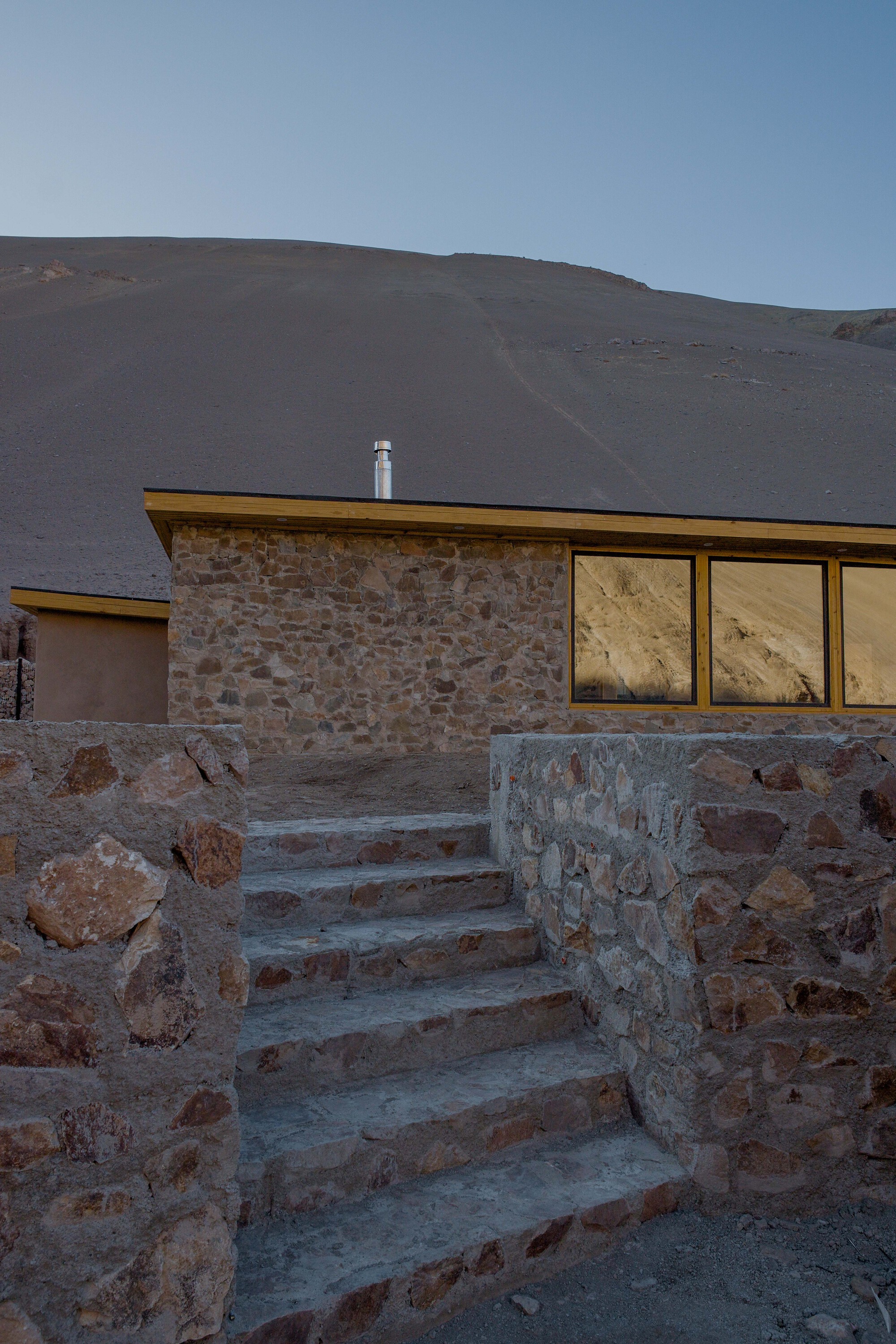 Stone staircase ascending to the flat-roofed structure with ribbon windows at twilight