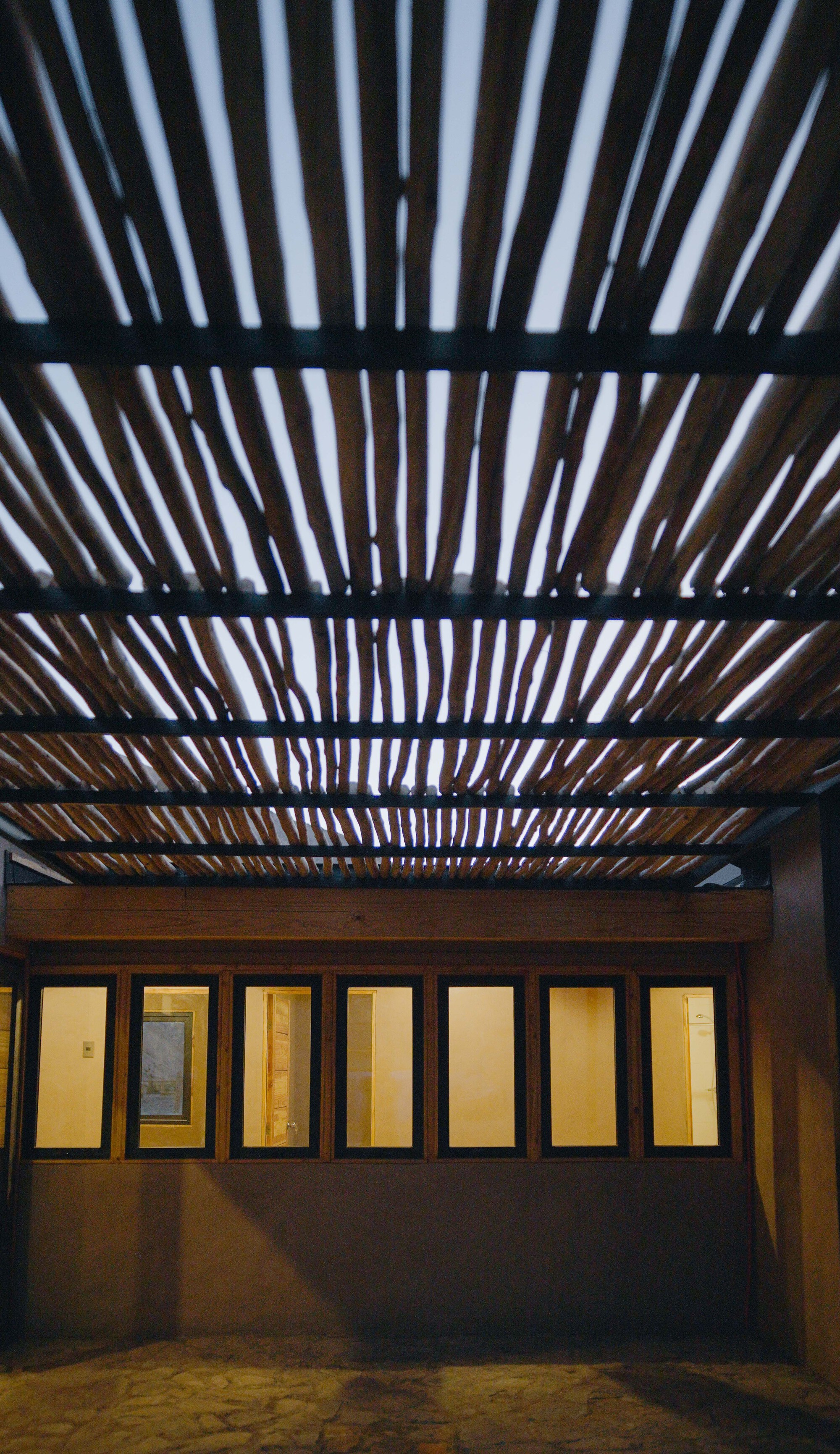 Courtyard view of timber pergola above illuminated glazed doors in the evening