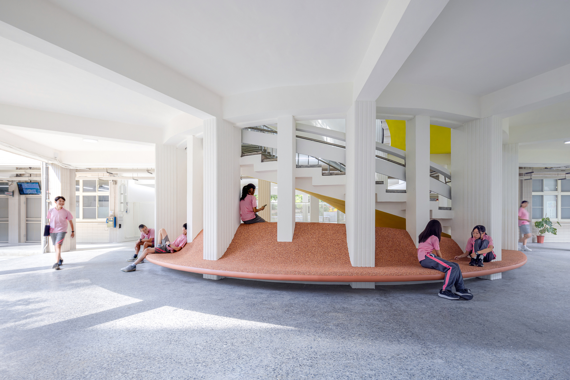 Students gathered on the terraced cork seating platform beneath white columns and exposed ductwork