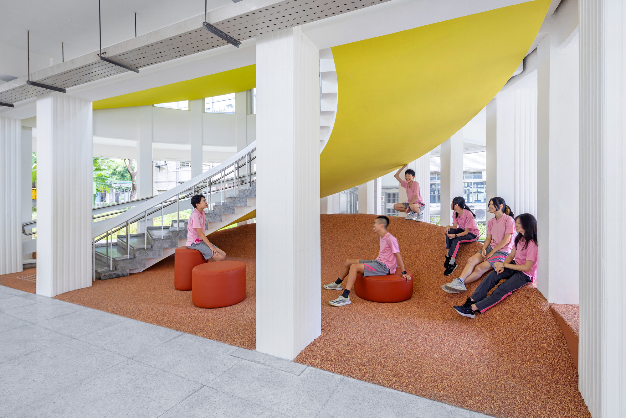 Cork terrazzo seating landscape with yellow ceiling panels and orange upholstered stools beside the staircase