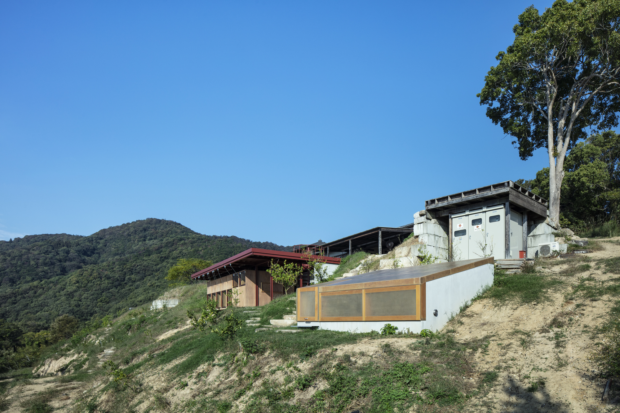 Compound of stepped volumes on grassy slope with forested hills in the background