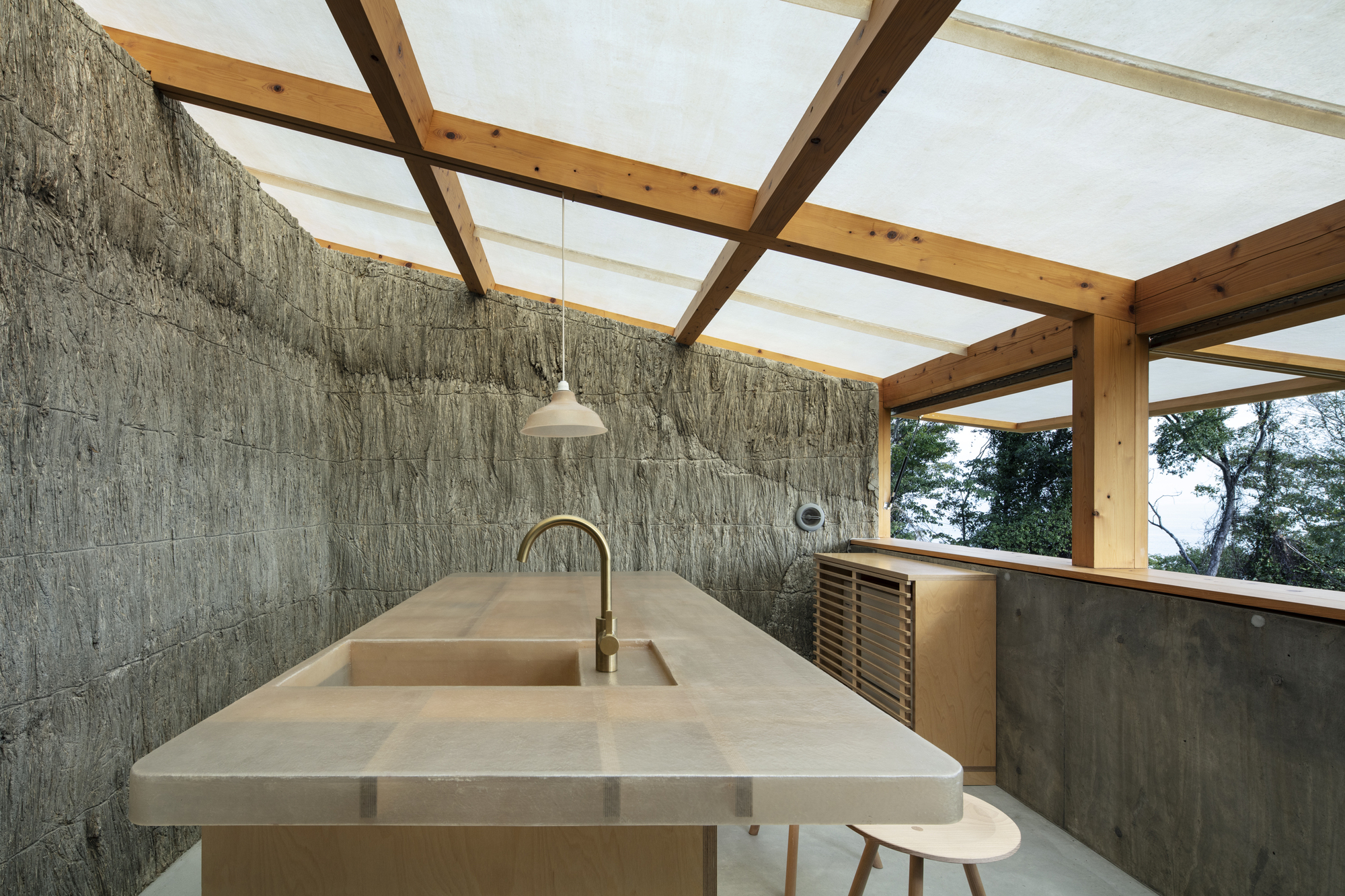Kitchen counter with stone surface under exposed timber rafters and translucent skylight panels