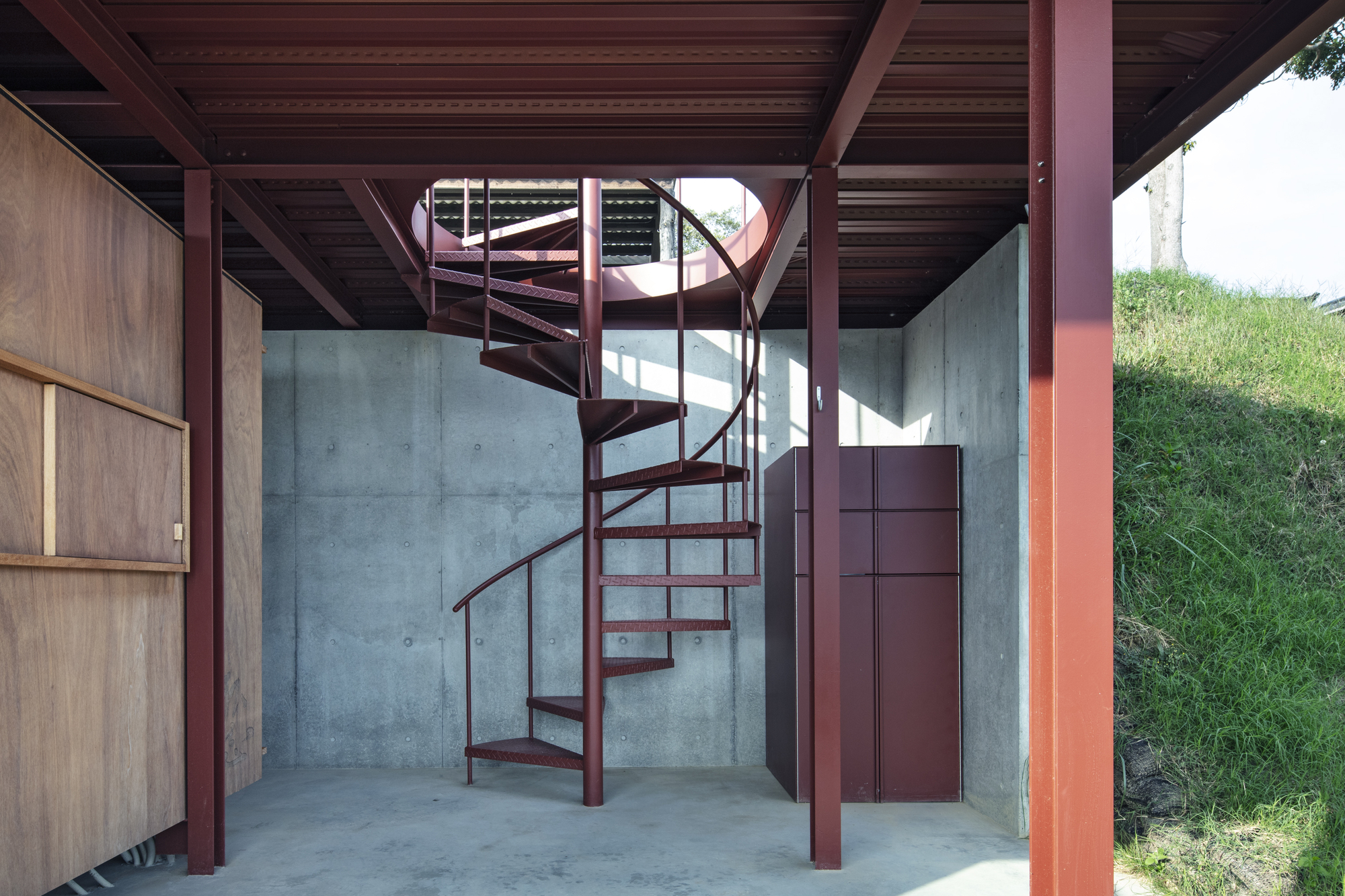 Red spiral stair rising through space with exposed steel columns and concrete walls