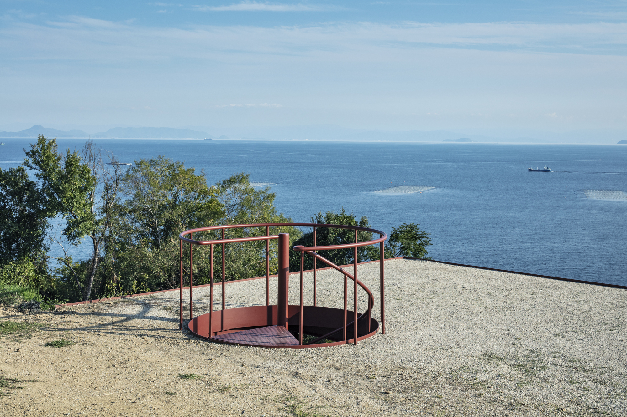 Circular steel-framed observation platform on the gravel terrace with ocean views beyond