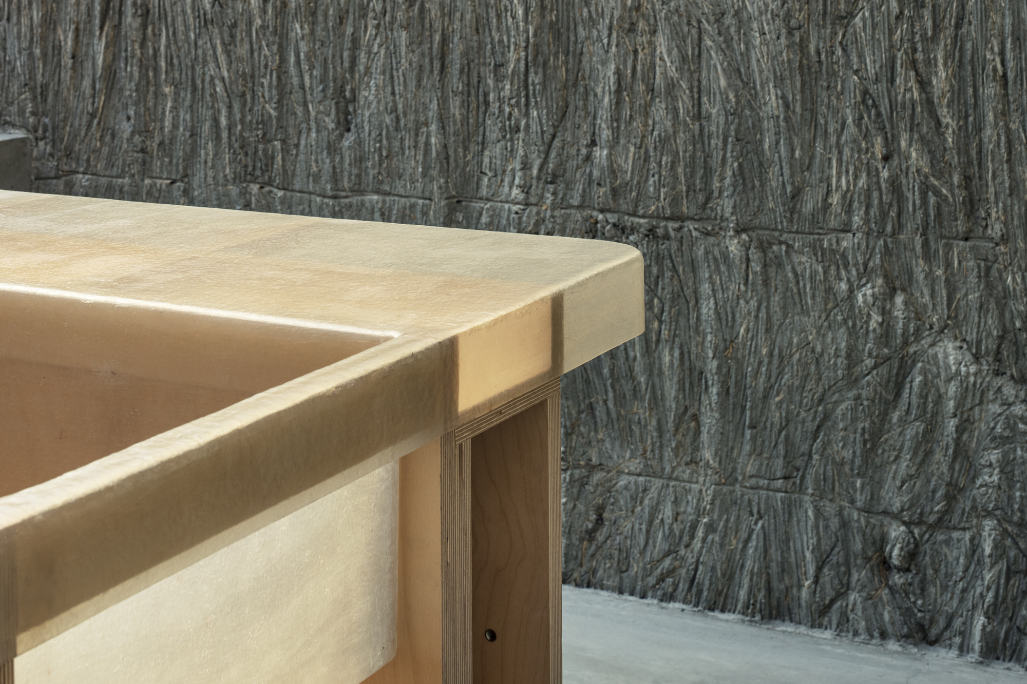 Detail of plywood countertop edge against rough-textured vertical concrete block wall