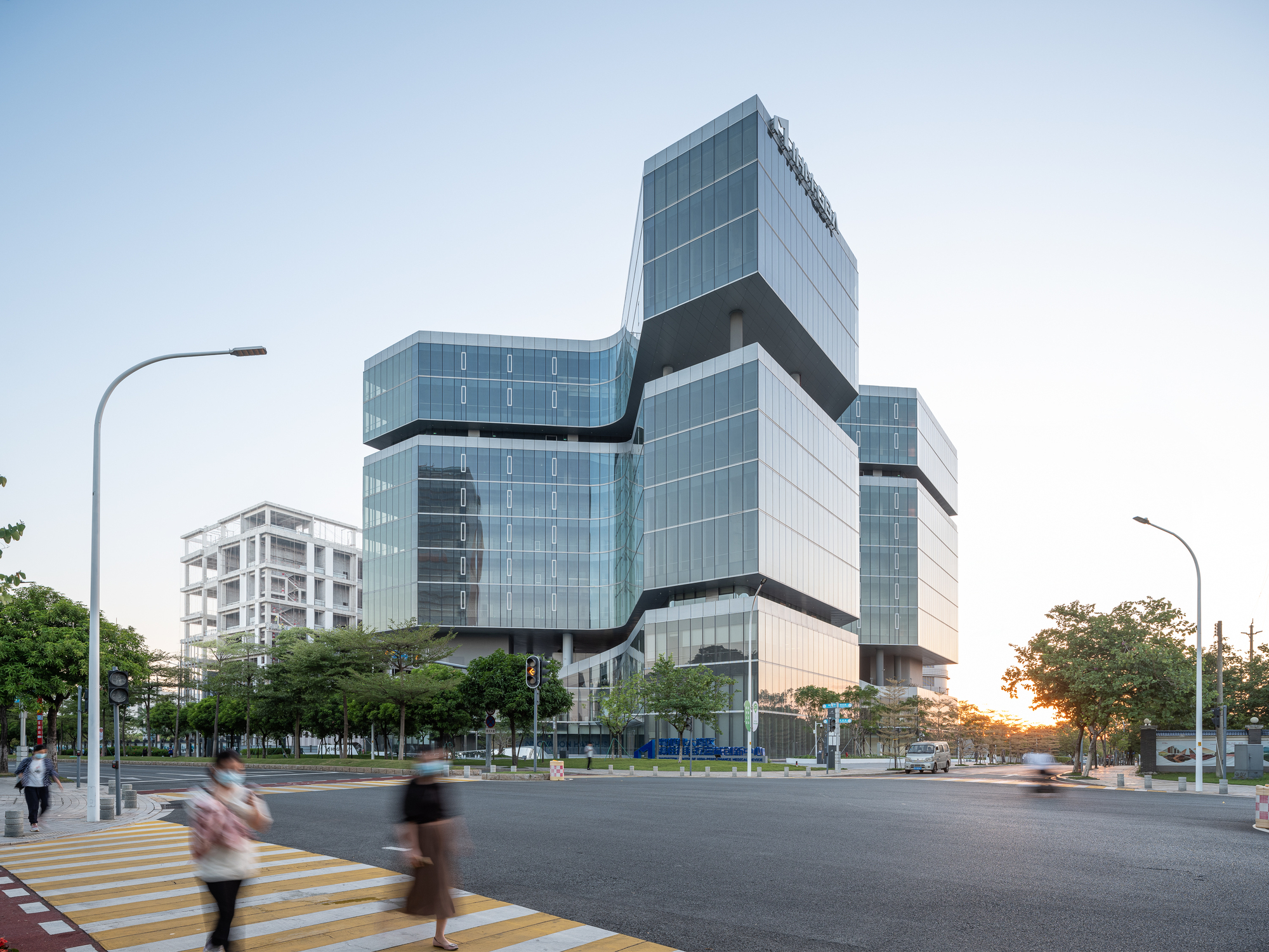 Stacked glass volumes wrapped with dark horizontal bands at an urban intersection at dusk
