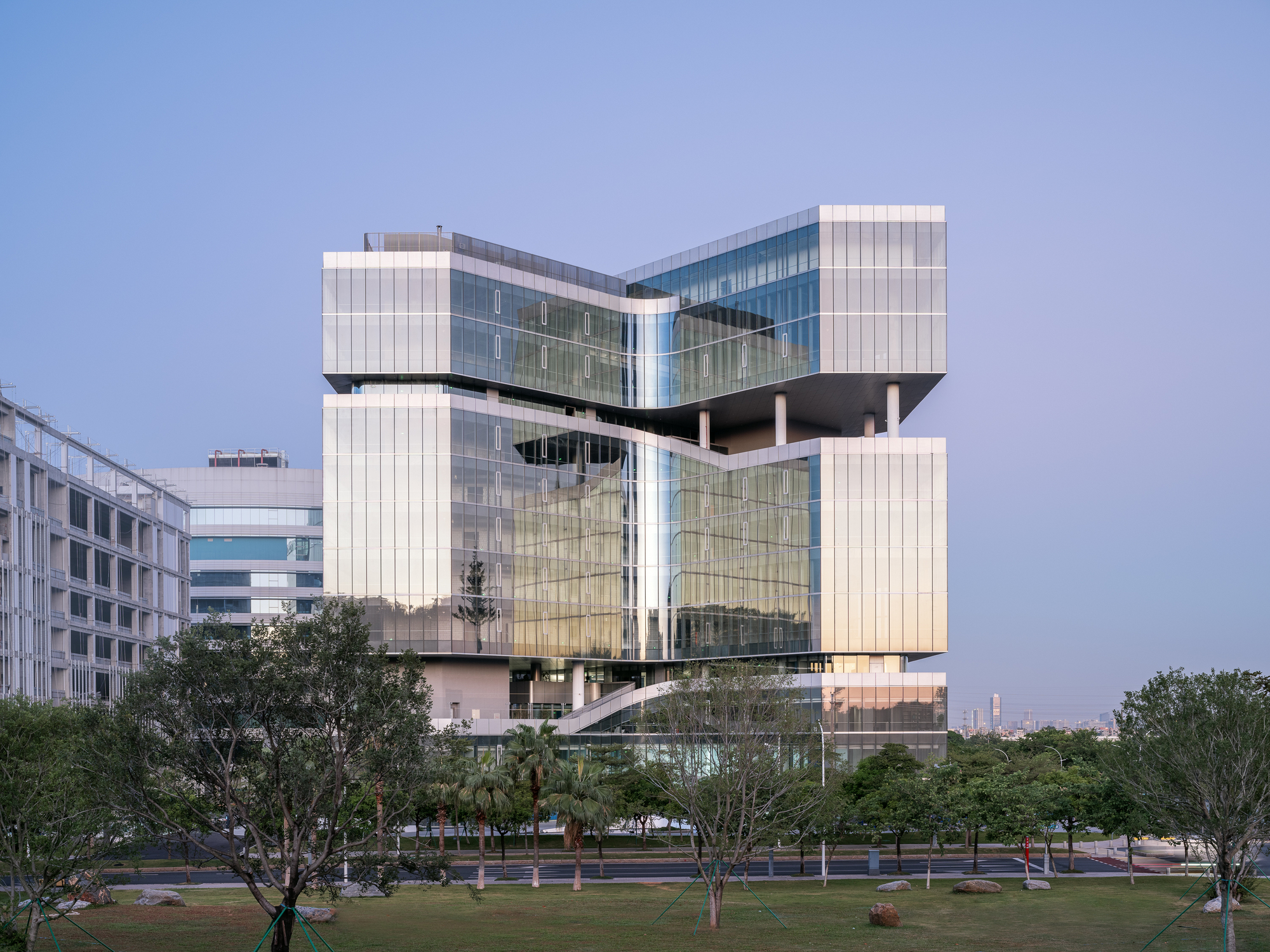 Illuminated facade composed of vertical white panels and floor-to-ceiling glass at twilight