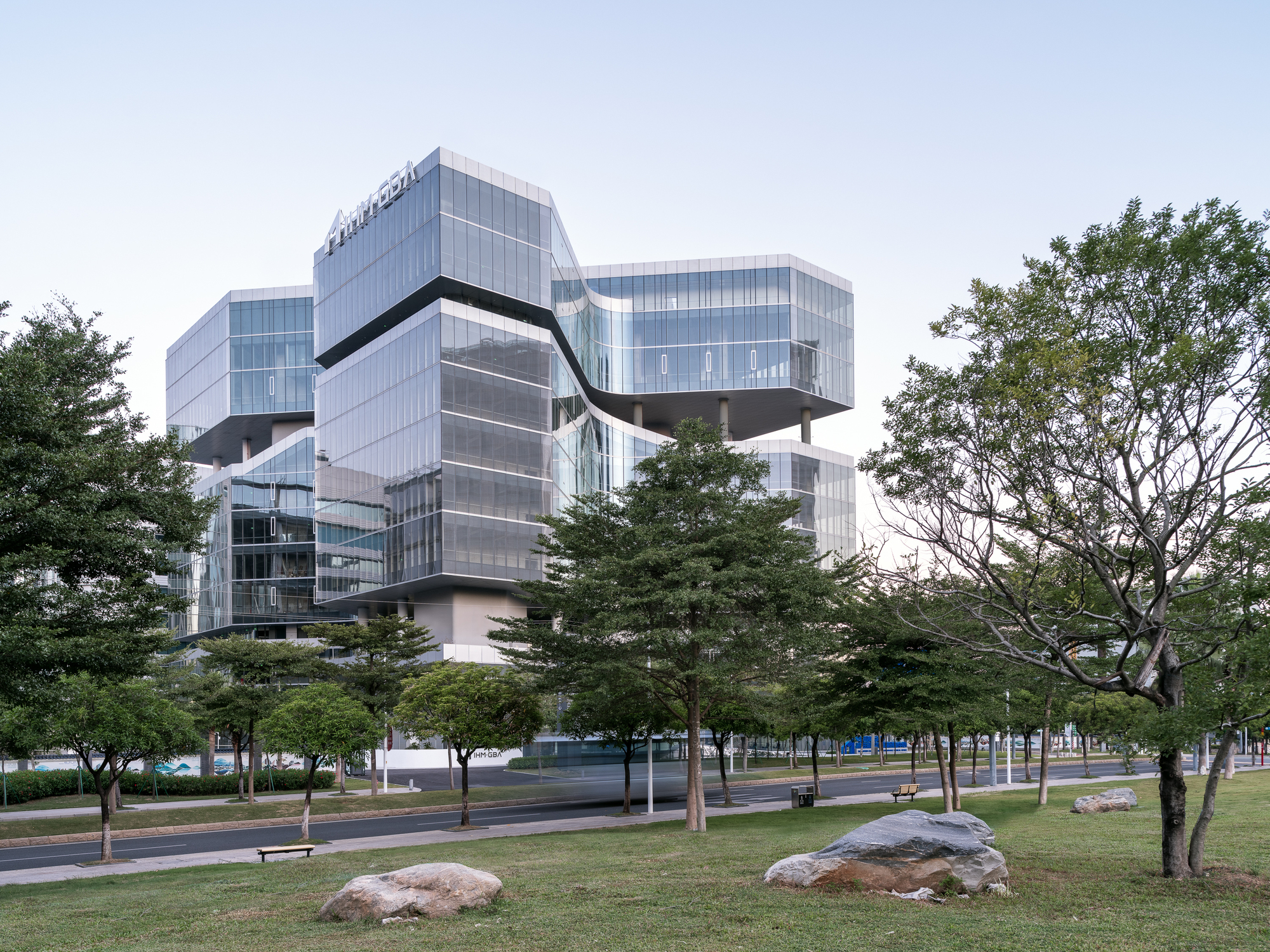 Cantilevered volumes rising above tree-lined plaza under overcast sky