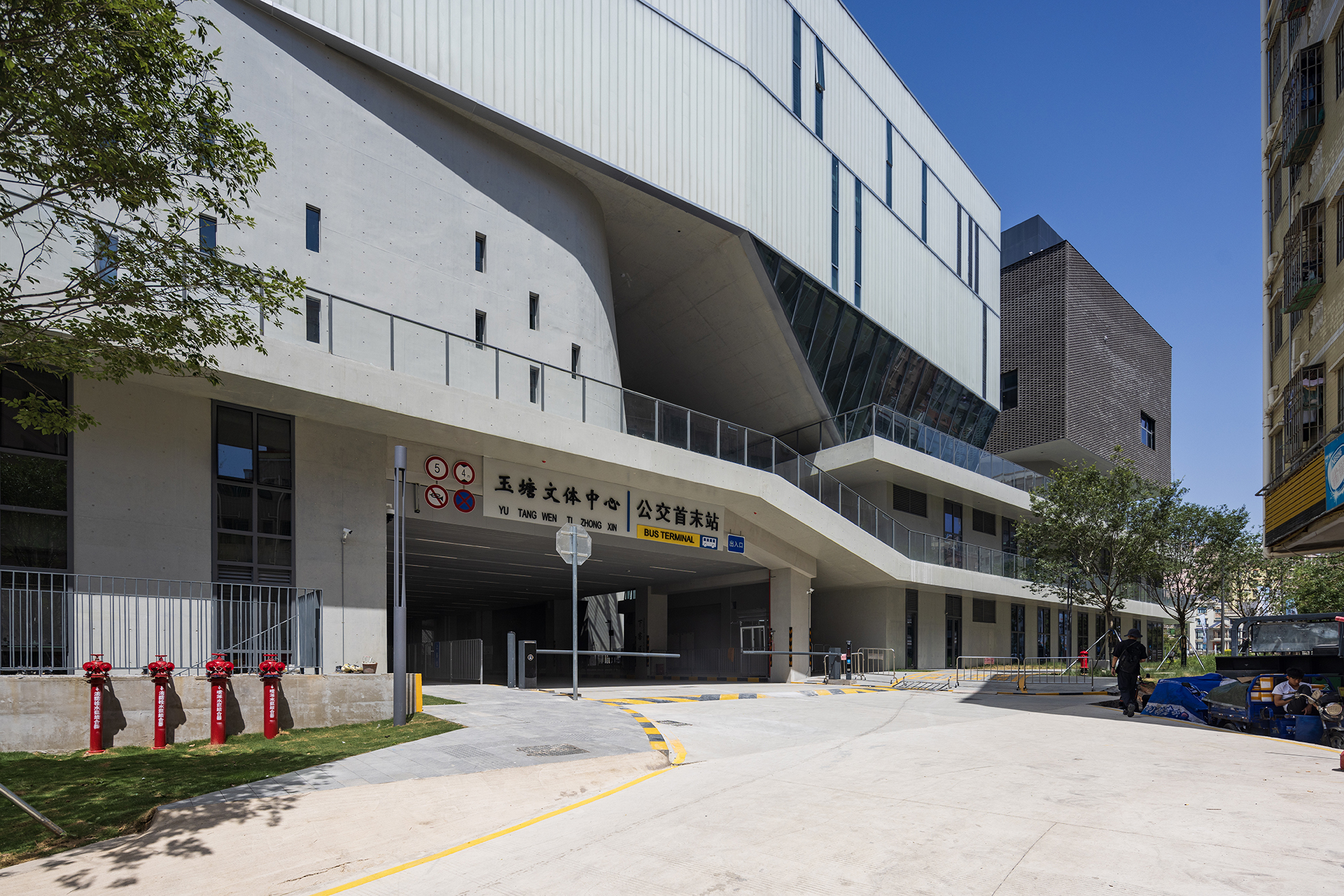 Covered entrance driveway with exposed concrete ceiling flanked by white metal cladding under clear blue sky
