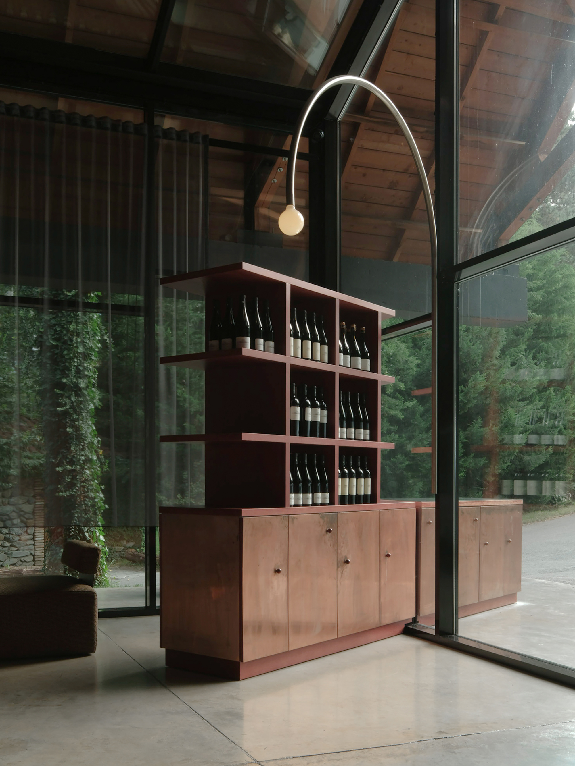 Freestanding wine shelving unit in pink-stained plywood with arched floor lamp