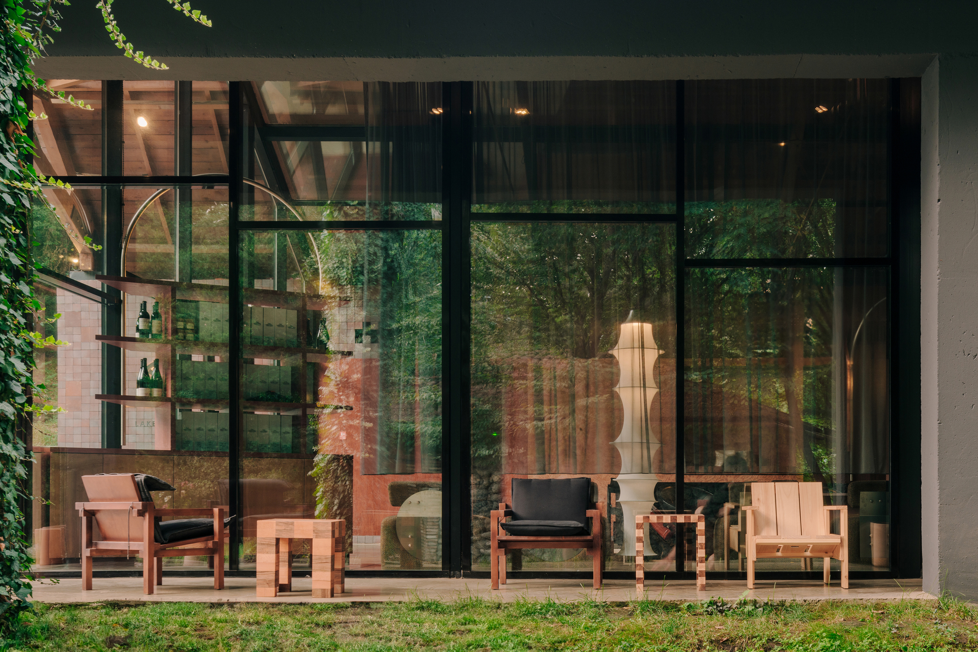 Garden view through floor-to-ceiling steel-framed windows showing timber furniture and ivy climbing at dusk