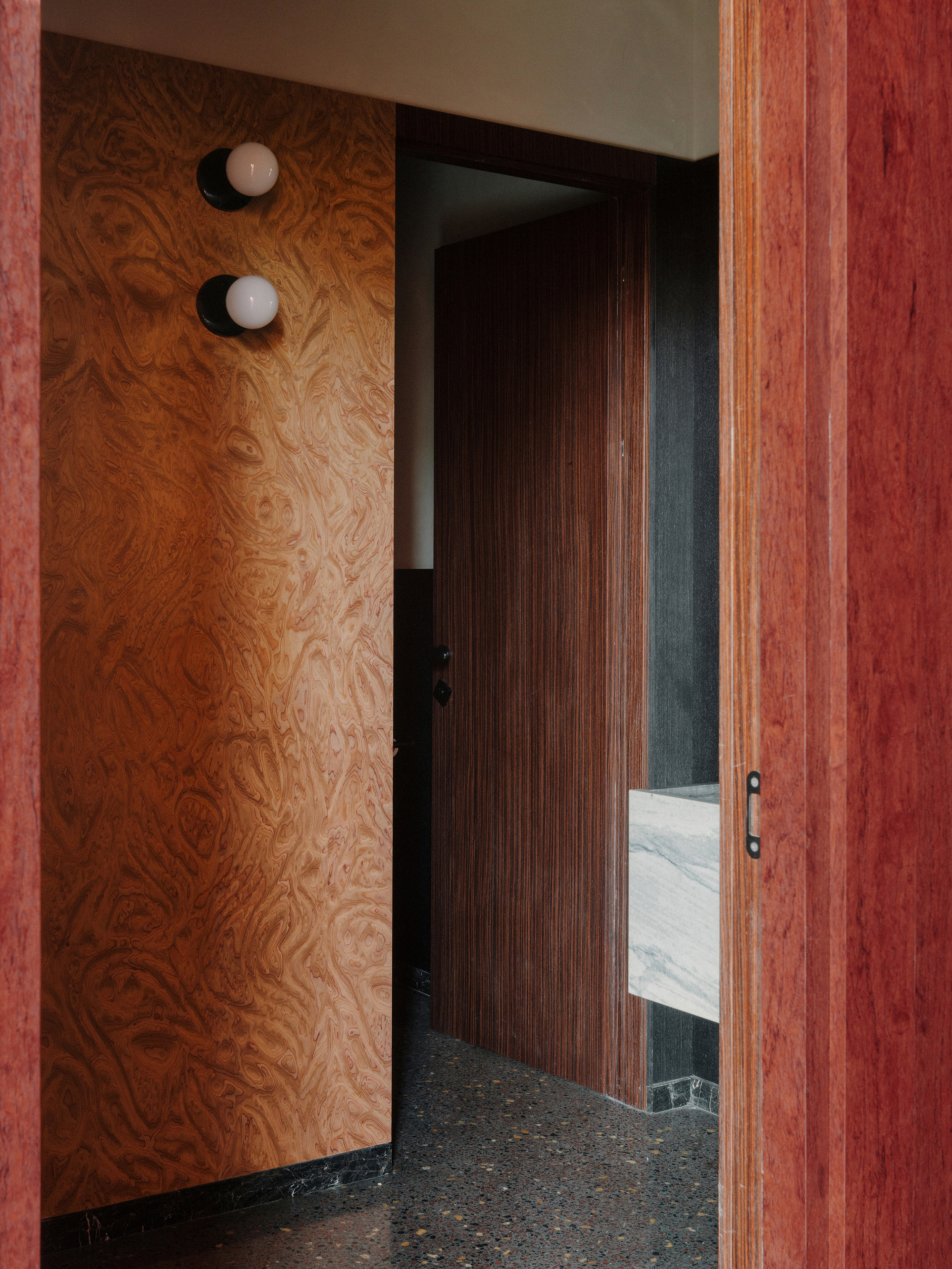 Plywood wall with two circular sconces beside a vertically grooved timber door