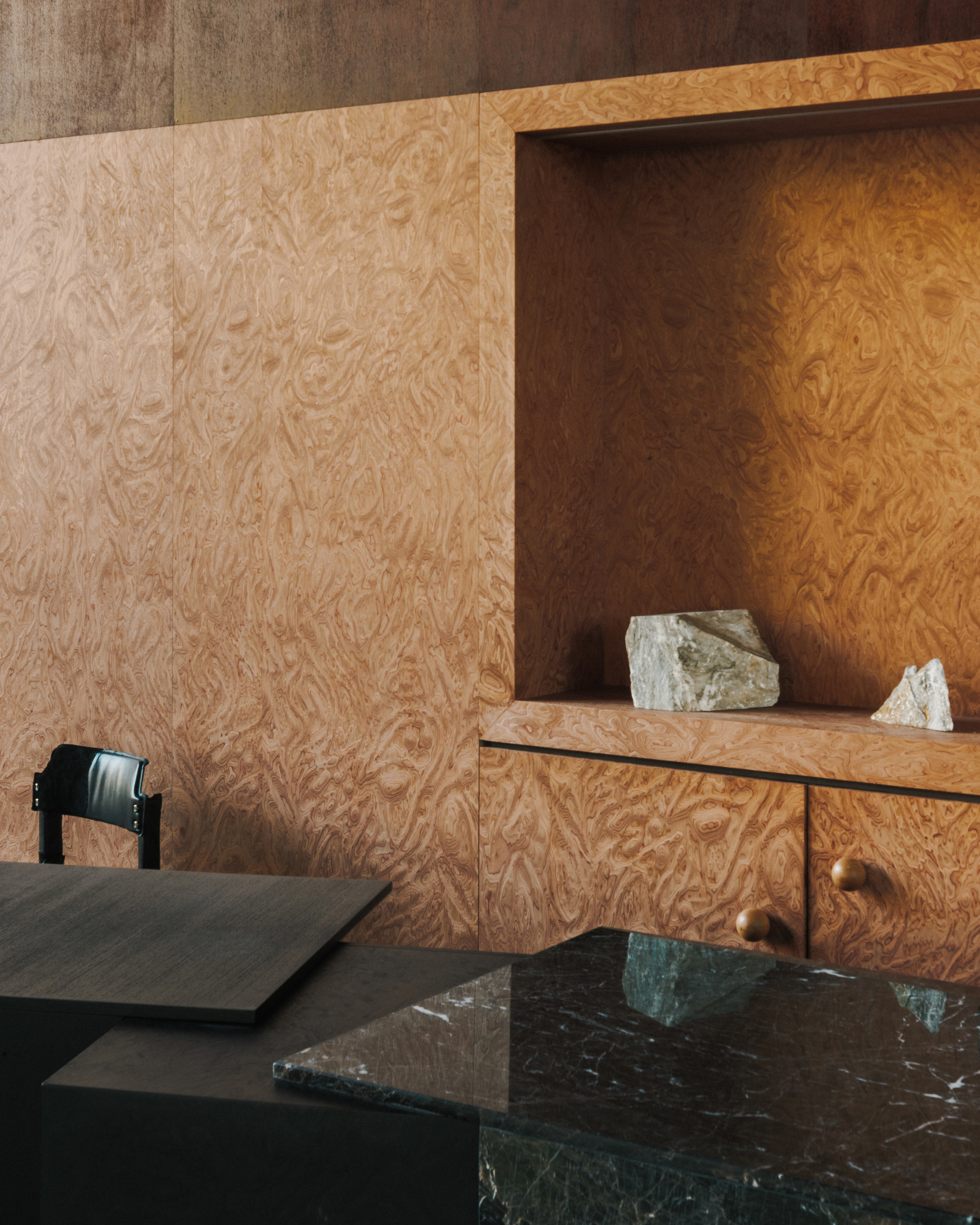 Burled wood wall panels with recessed niche and marble countertop overlooking a dark stone surface