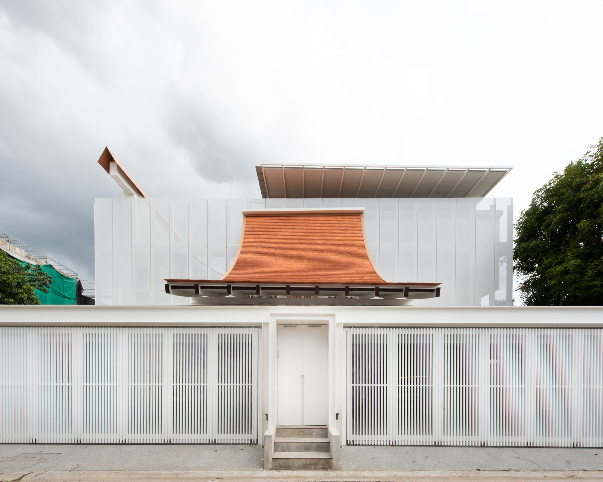 Street view of white vertical slat fence with central entry steps under a curved terracotta roof