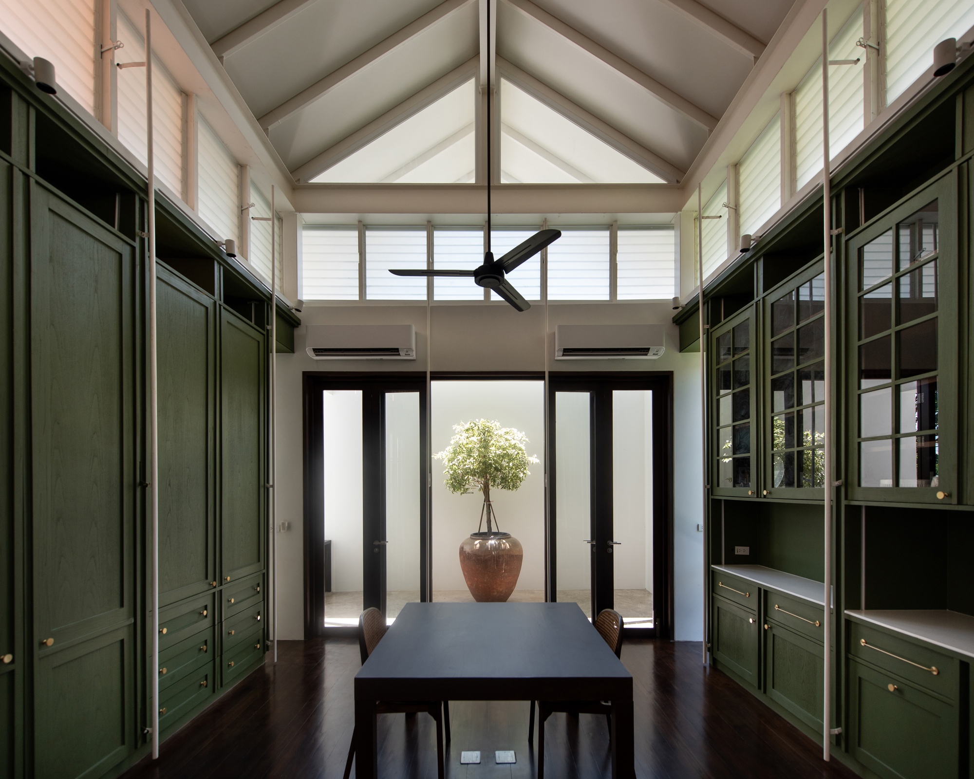Dining room framed by green built-in cabinetry beneath a vaulted ceiling with clerestory windows