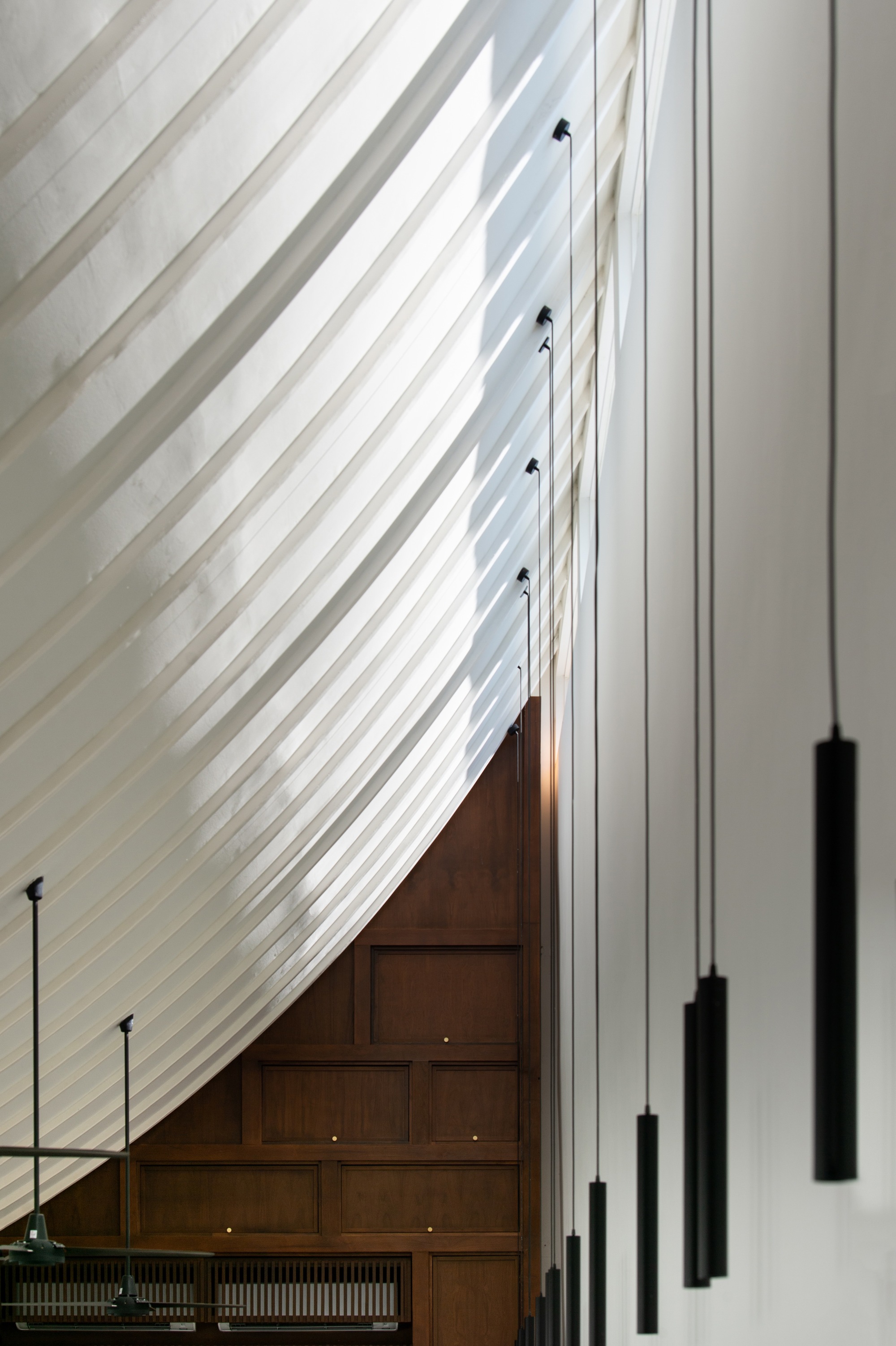 Double-height space with diagonal white slat wall and suspended black cylindrical pendant lights