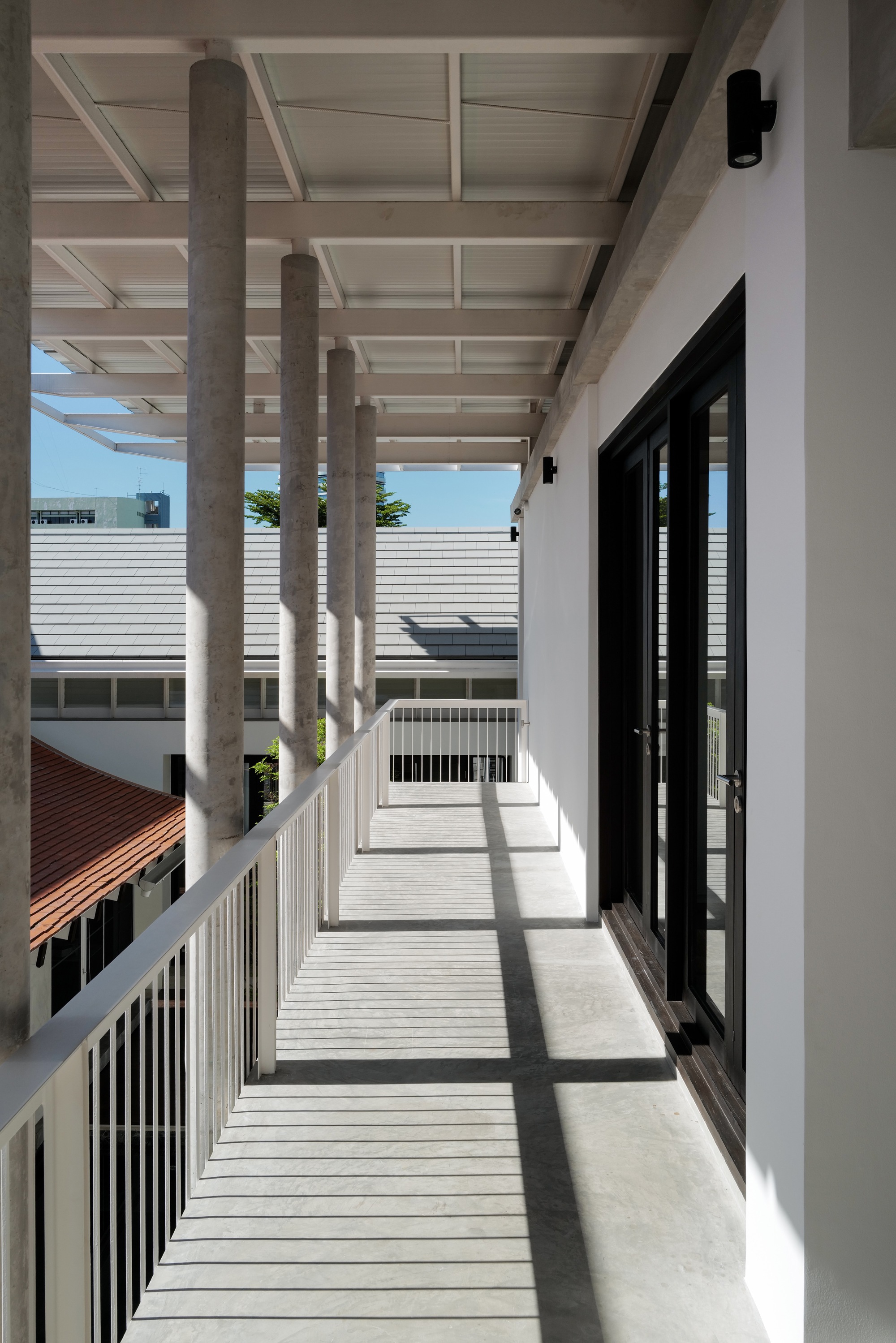 Upper-level walkway with exposed concrete columns casting shadows across slatted timber decking in daylight