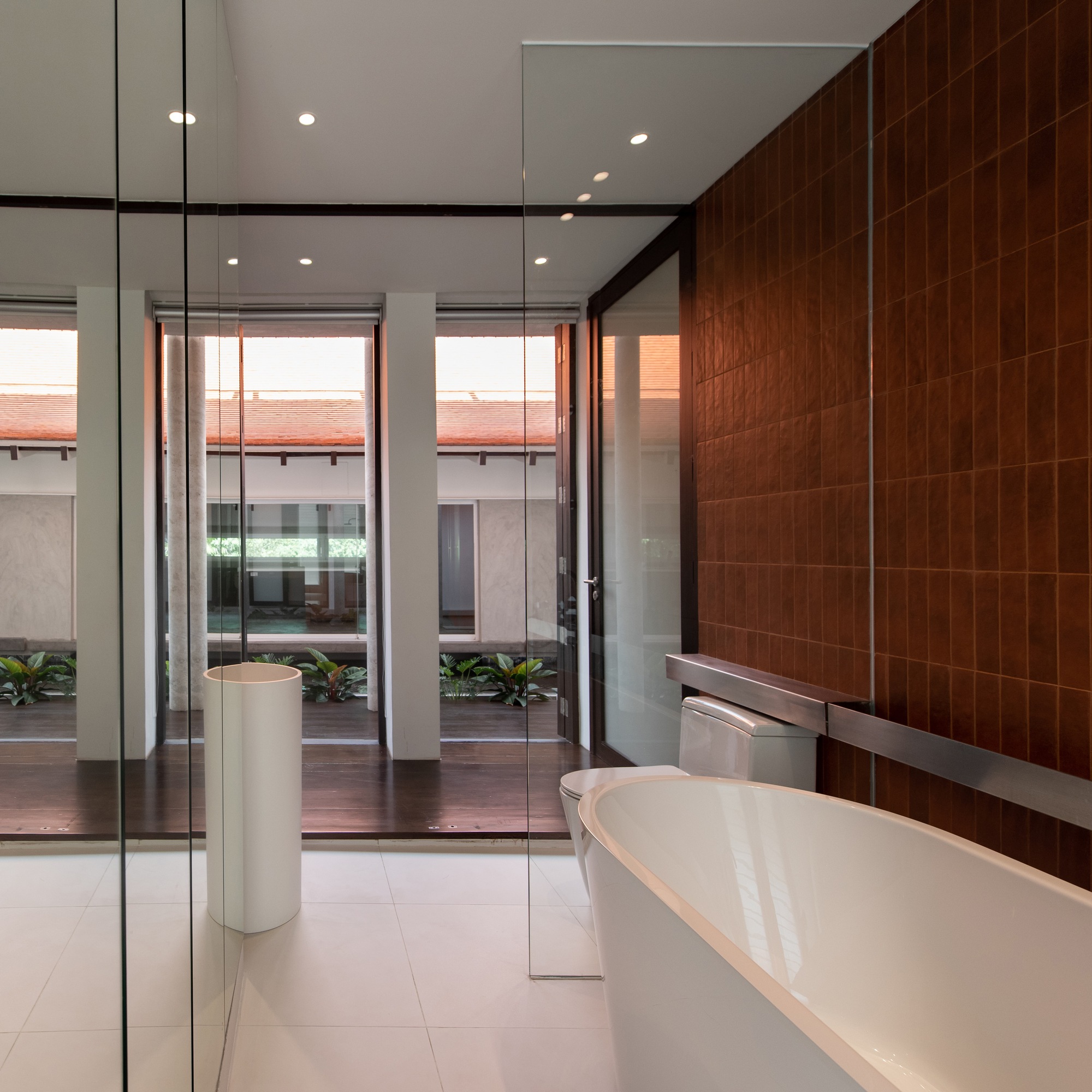 Bathroom with freestanding white tub and wood tile wall looking onto a planted courtyard
