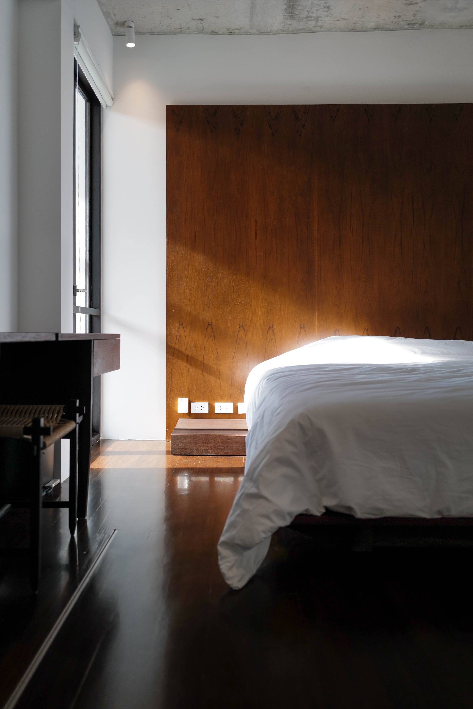 Bedroom with timber paneled wall illuminated by morning sunlight from a narrow window