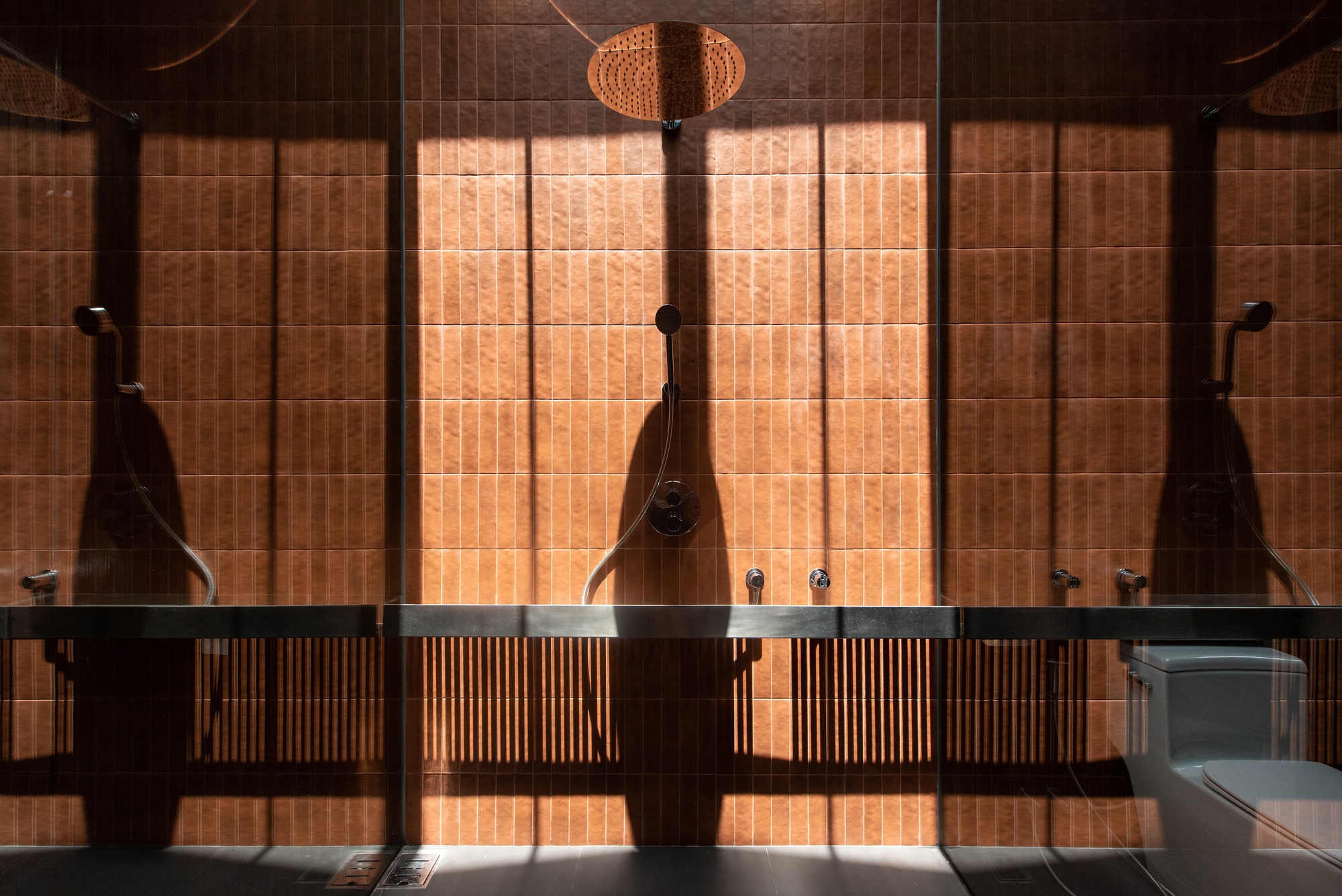 Bathroom with illuminated terracotta tile wall reflected in full-height mirror with slatted wooden screen below