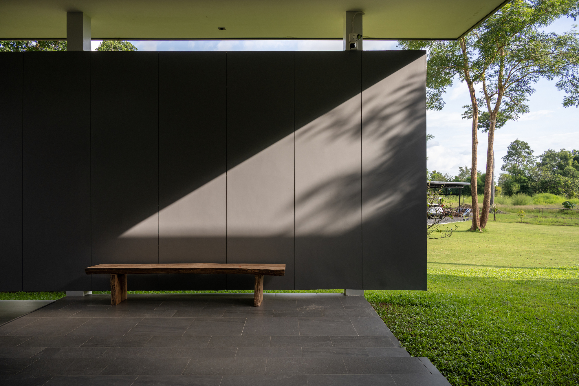 Covered terrace with dark panel wall and timber bench facing open lawn