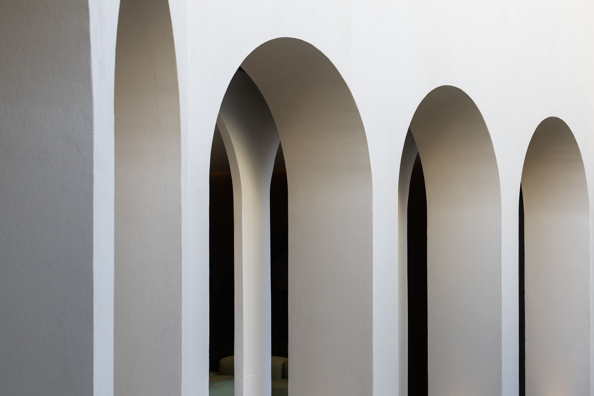 Sequence of tall arched openings with smooth plaster reveals receding into shadow