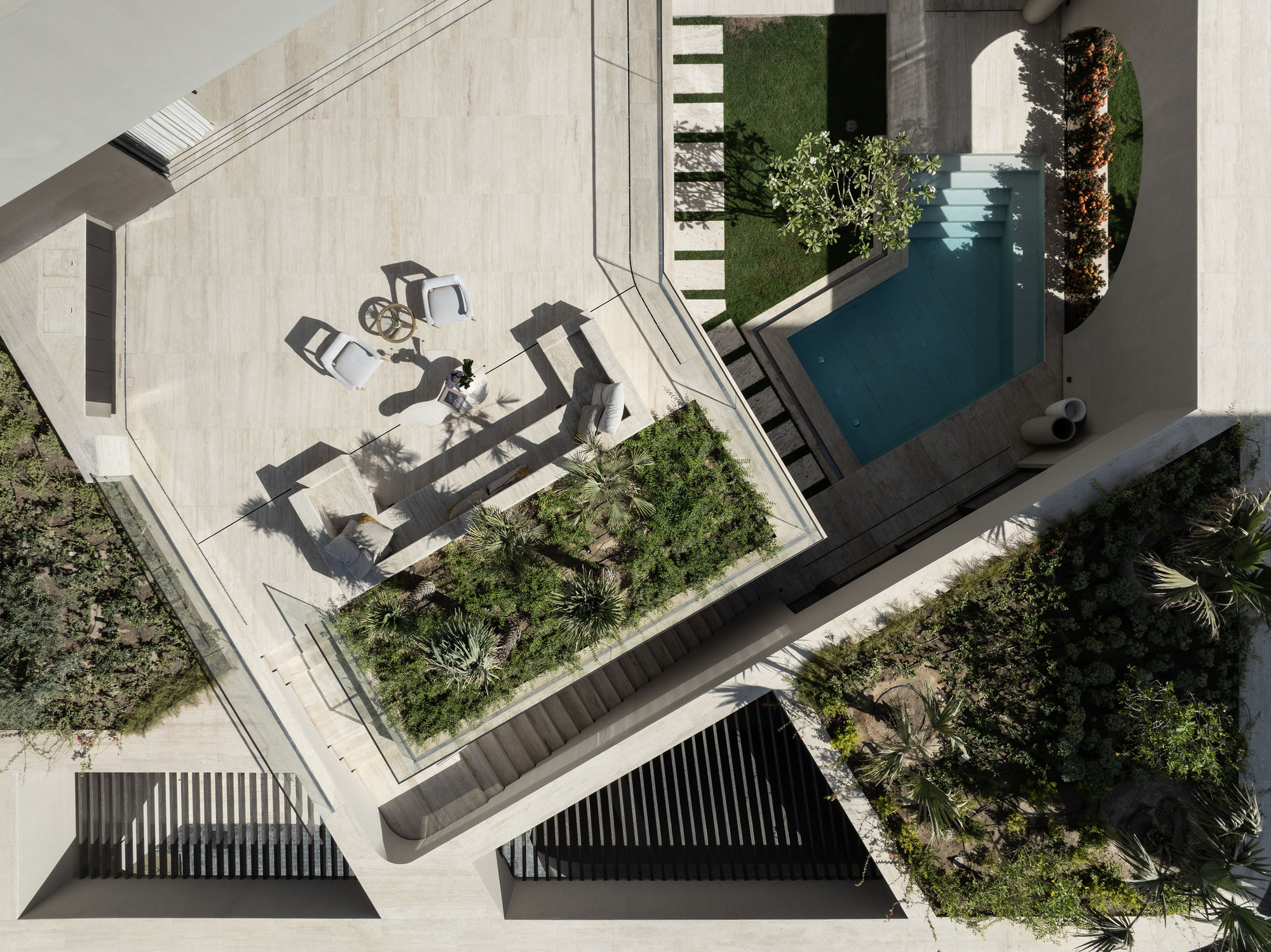 Aerial view of terraced courtyards with pool and outdoor furniture casting long shadows