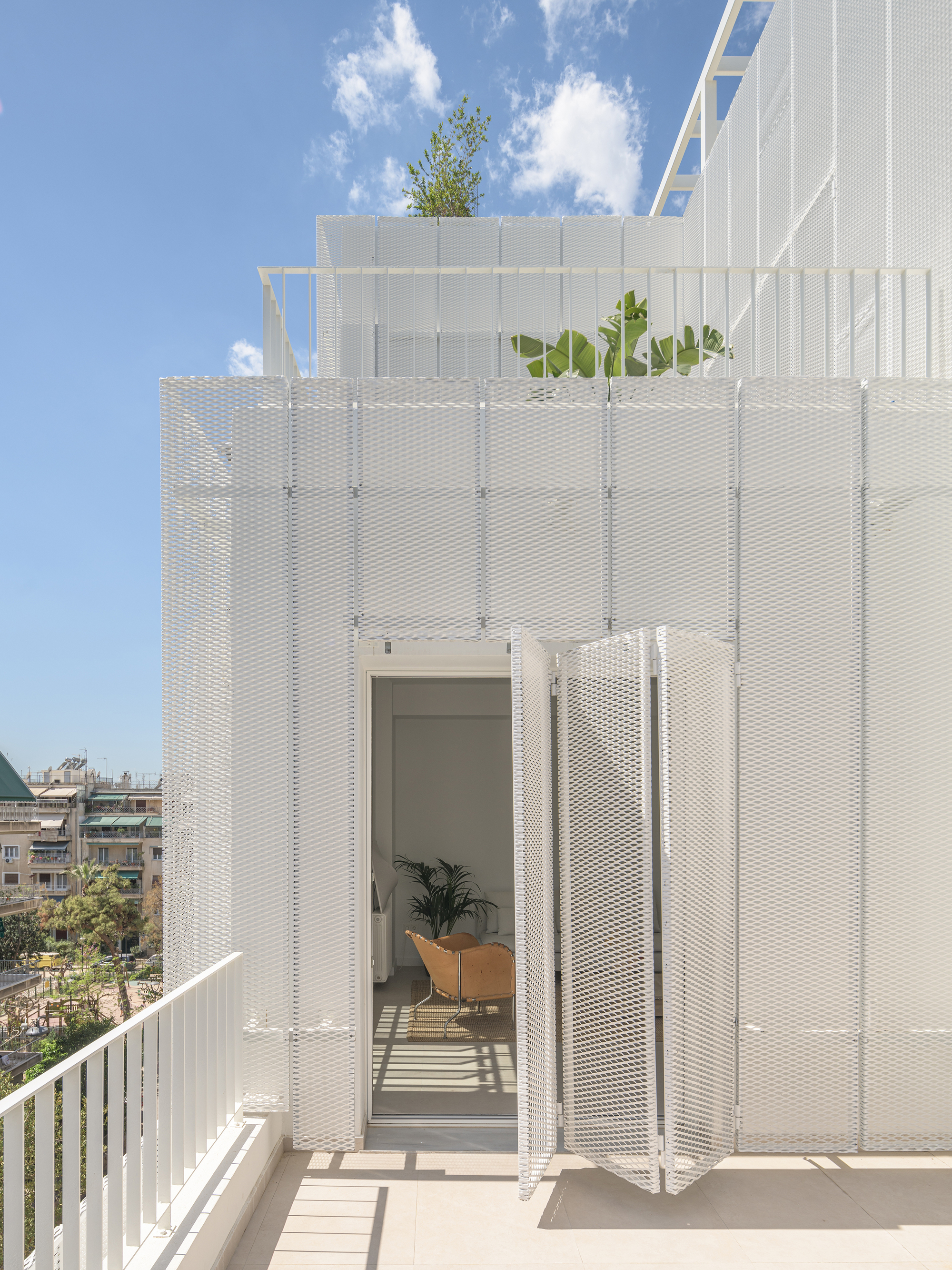 Rooftop terrace with white perforated metal screens, planted bed, and sliding glass door beneath clouds