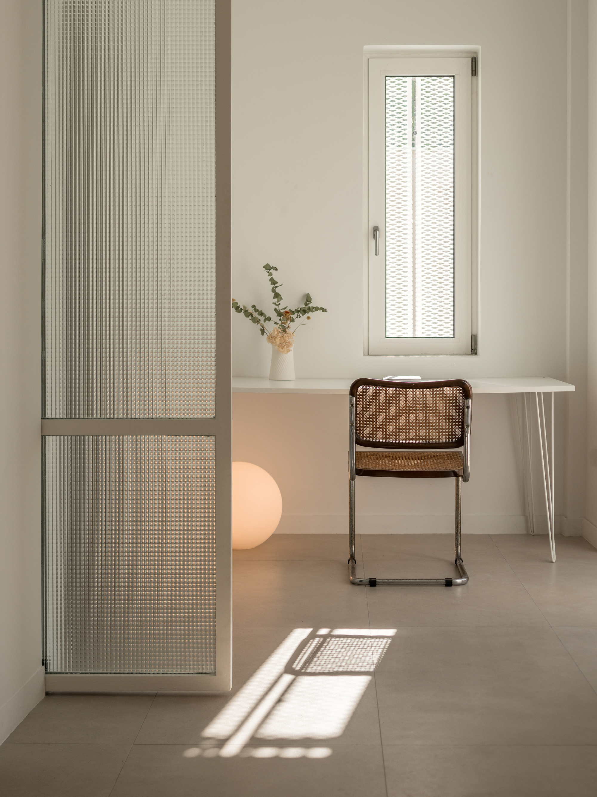 Interior room with perforated sliding panels, work desk, and cane chair bathed in afternoon sunlight