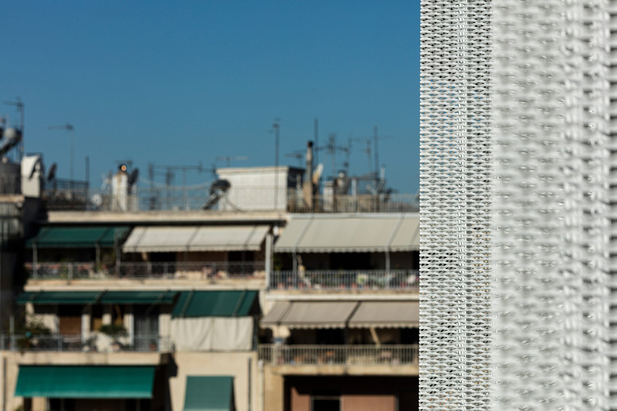 Detail of the textured white screen facade against older residential balconies in the background