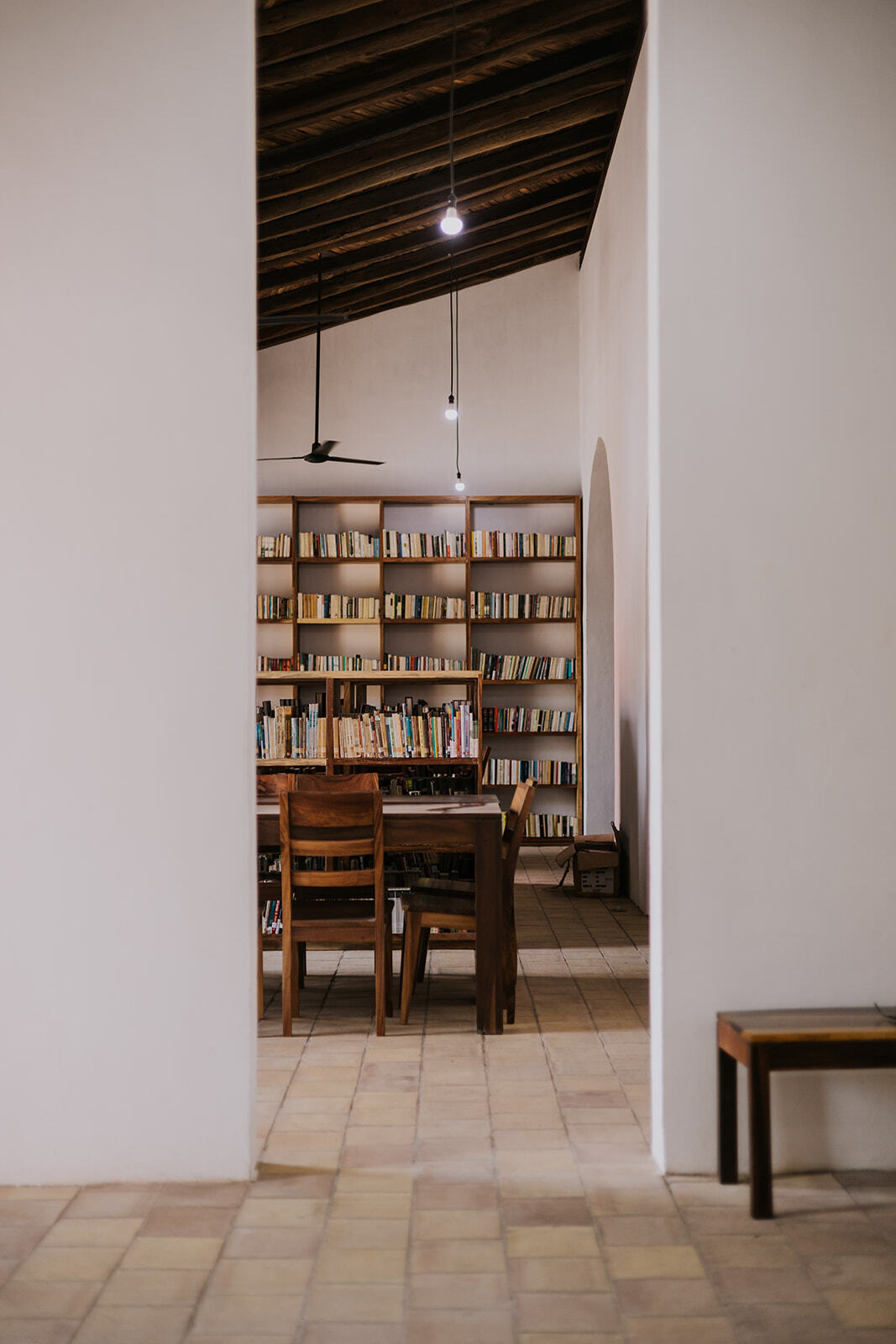 Timber dining table and chairs beside a bookshelf under an exposed rafter ceiling
