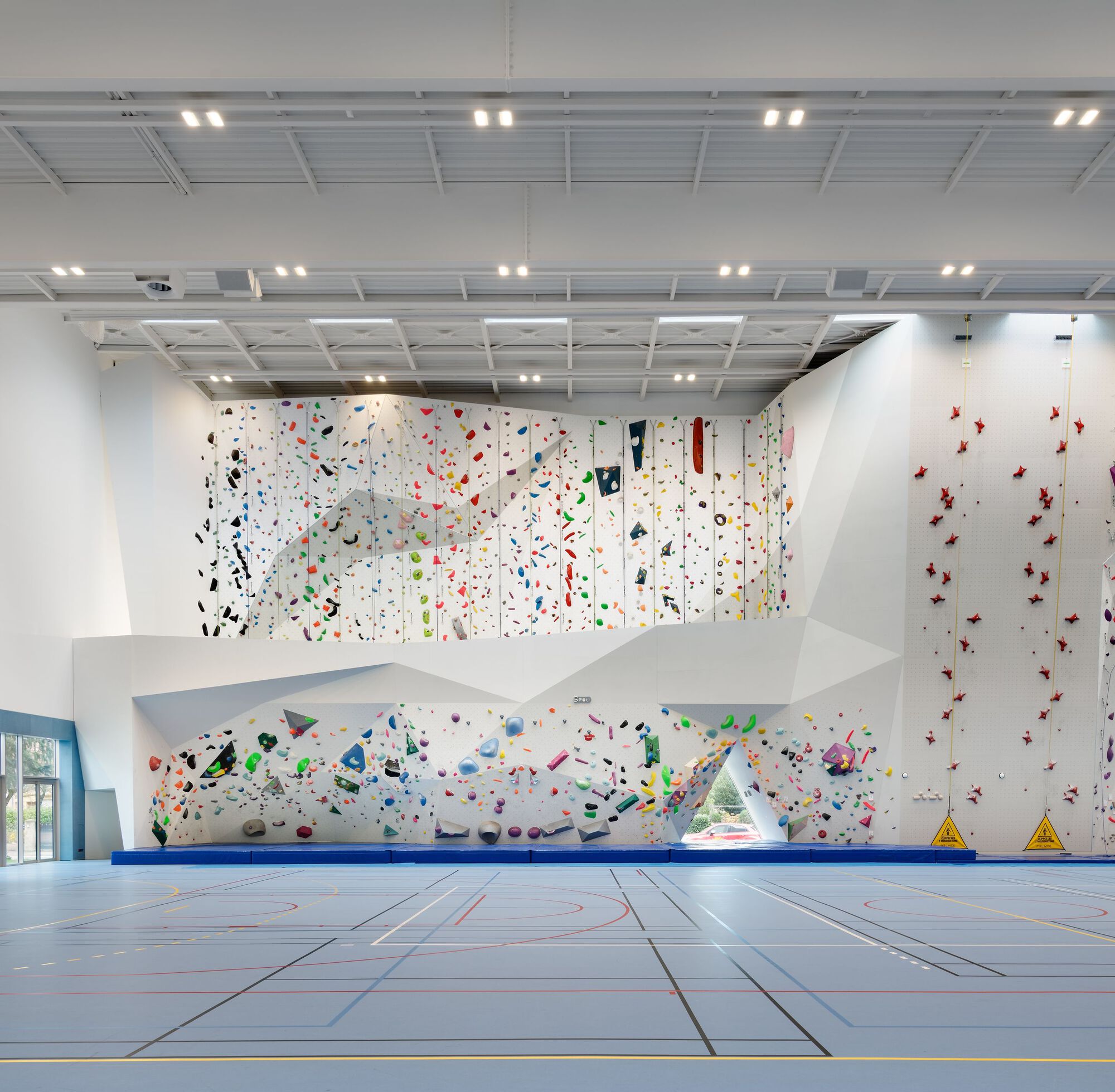 Two-story climbing wall with colorful holds and horizontal white viewing platform