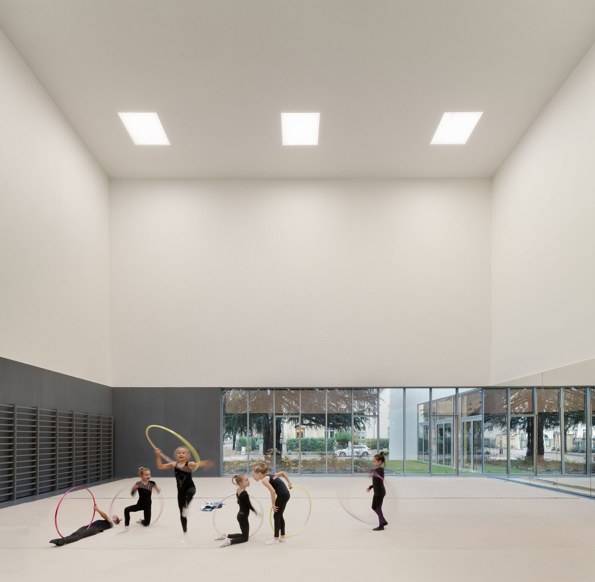 Rhythmic gymnastics studio with children practicing under three square skylights and glazed courtyard view