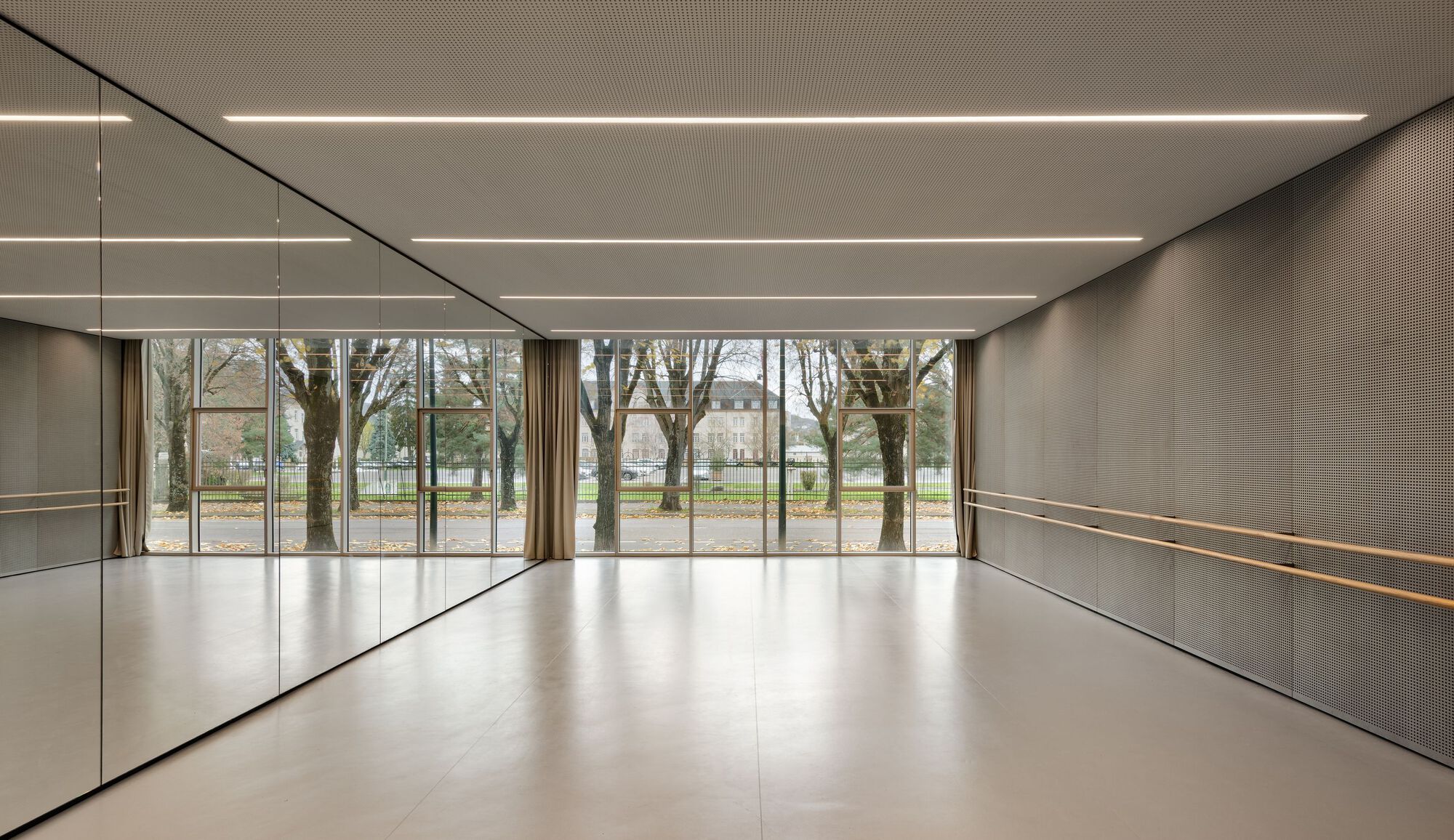 Dance studio with mirrored wall and horizontal light strips overlooking trees in a park