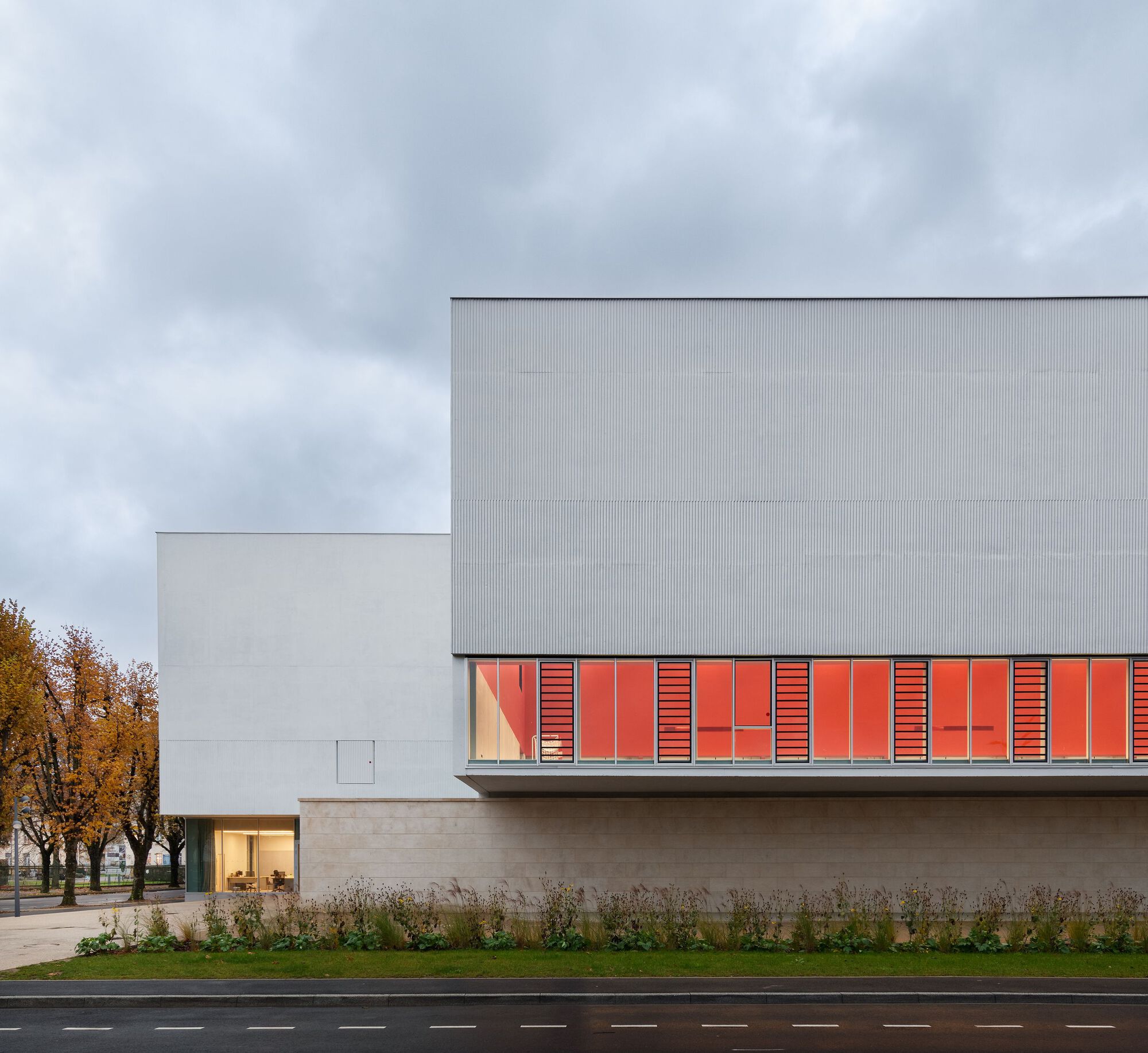 Street view of the corrugated metal facade with red louvered panels and autumn trees in the background