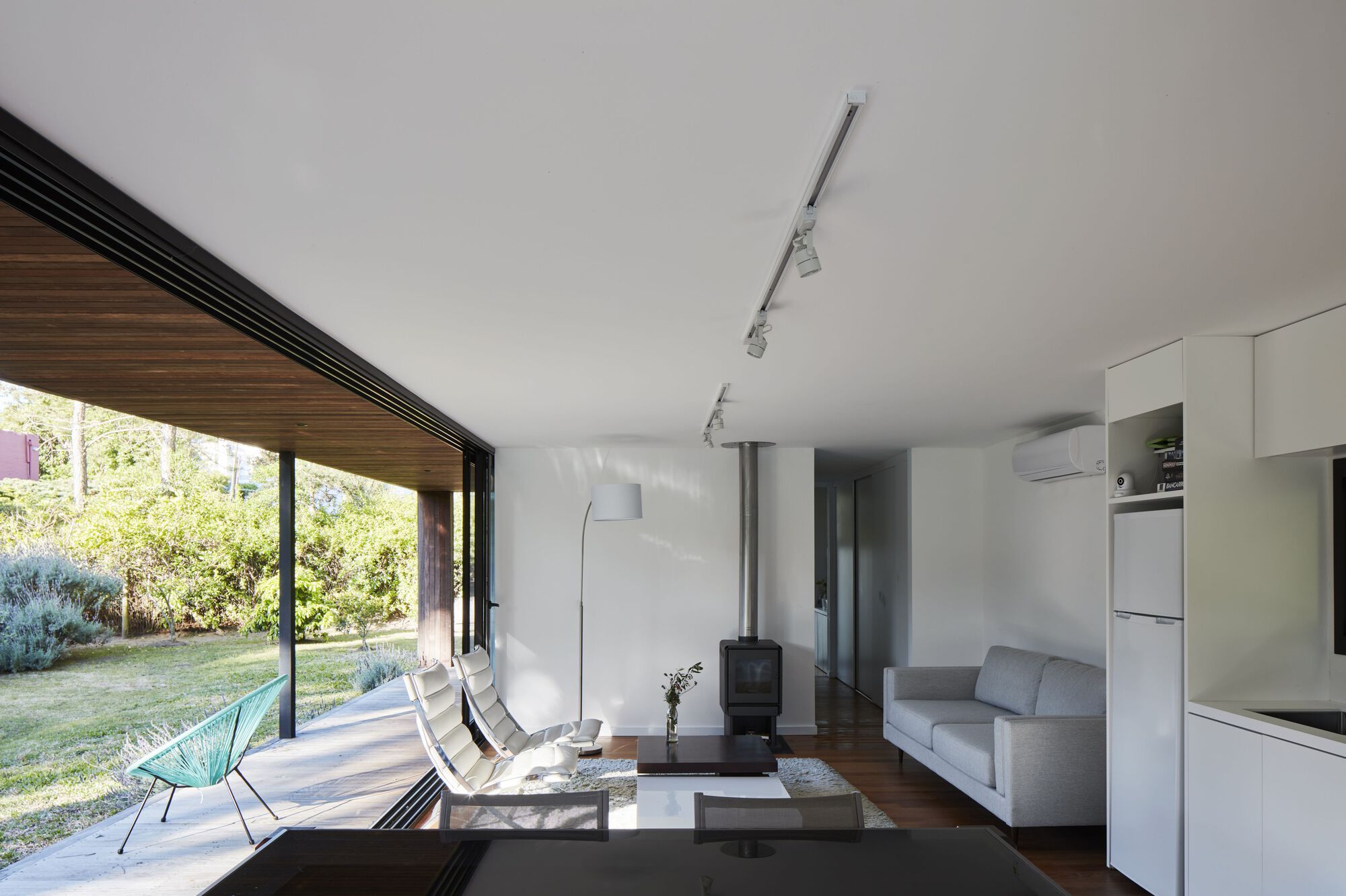 Interior living space with wood slat ceiling opening to garden through floor-to-ceiling glass