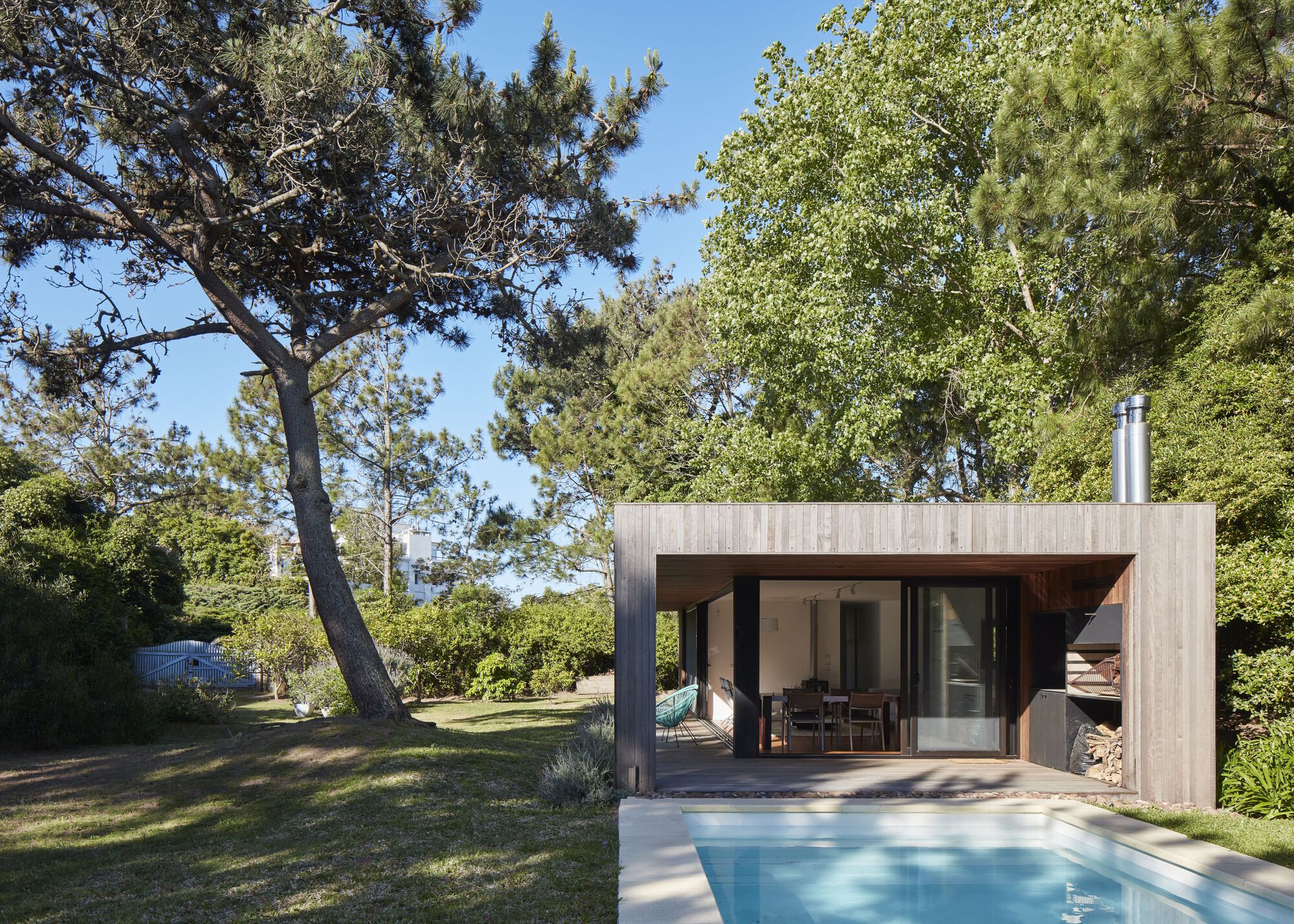 Pool terrace and flat-roofed pavilion with integrated firewood storage under afternoon sunlight