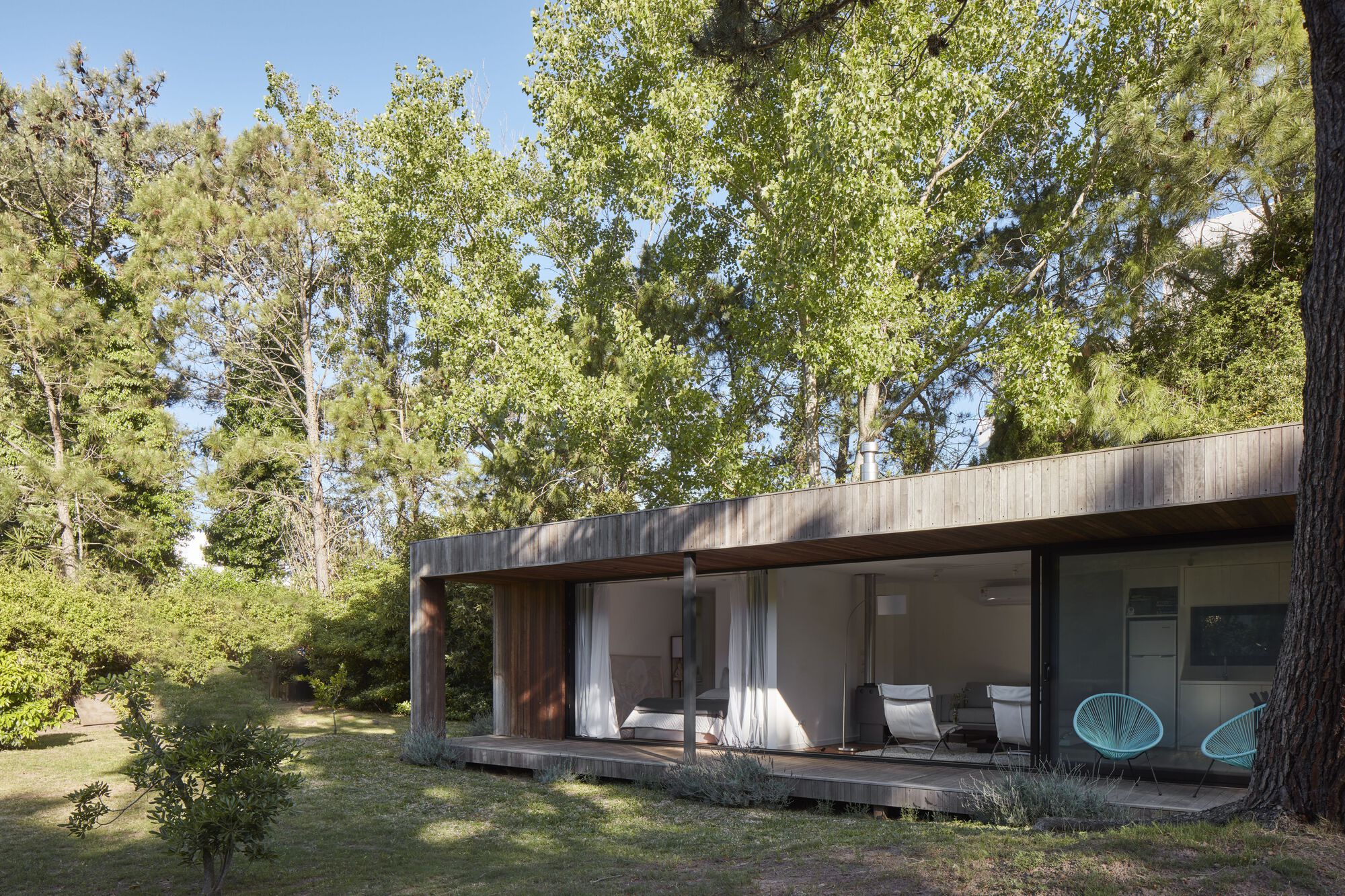 Garden view of the single-storey volume with sliding glass walls and timber-decked terrace